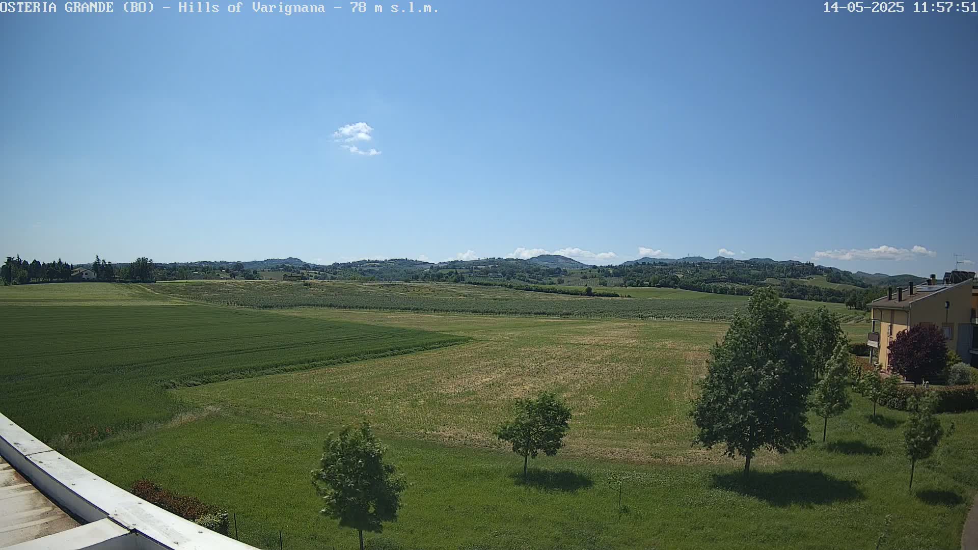 A sunny day reveals rolling green hills and fields, with a few trees and a building visible in the foreground.