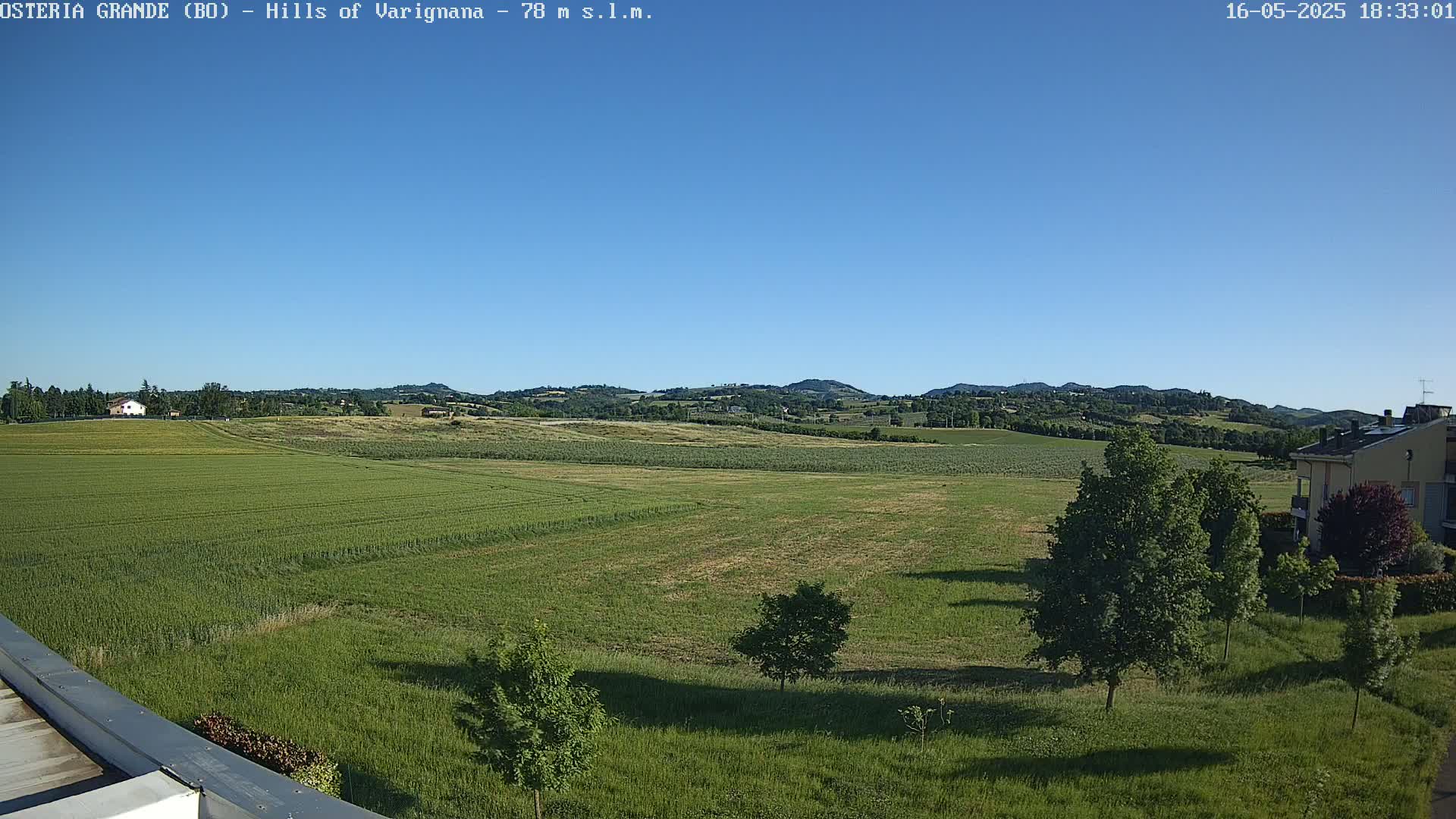 A sprawling green field dotted with trees extends to rolling hills under a clear blue sky.