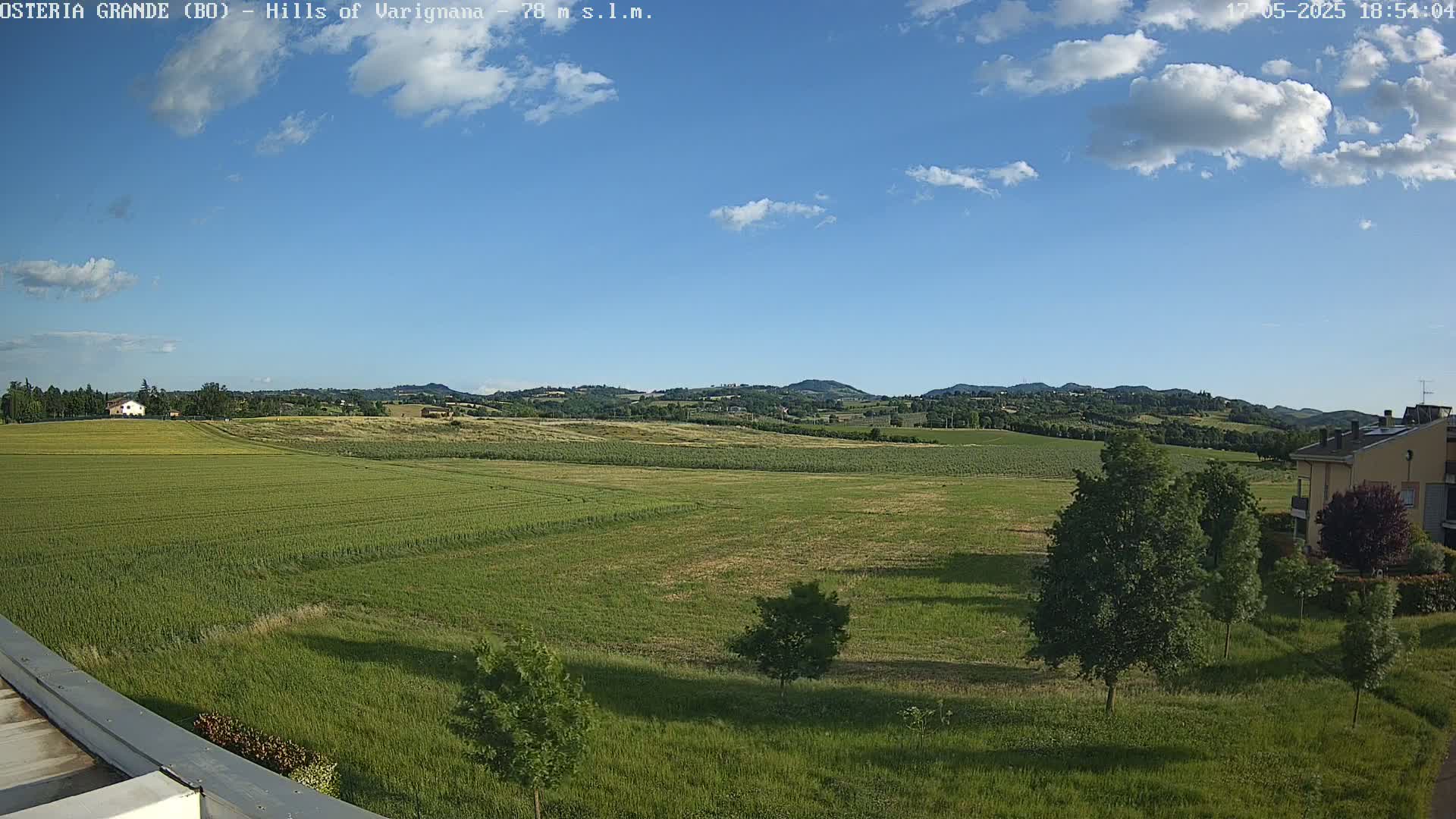 A partly cloudy blue sky overlooks a vast expanse of green fields and rolling hills in the distance.
