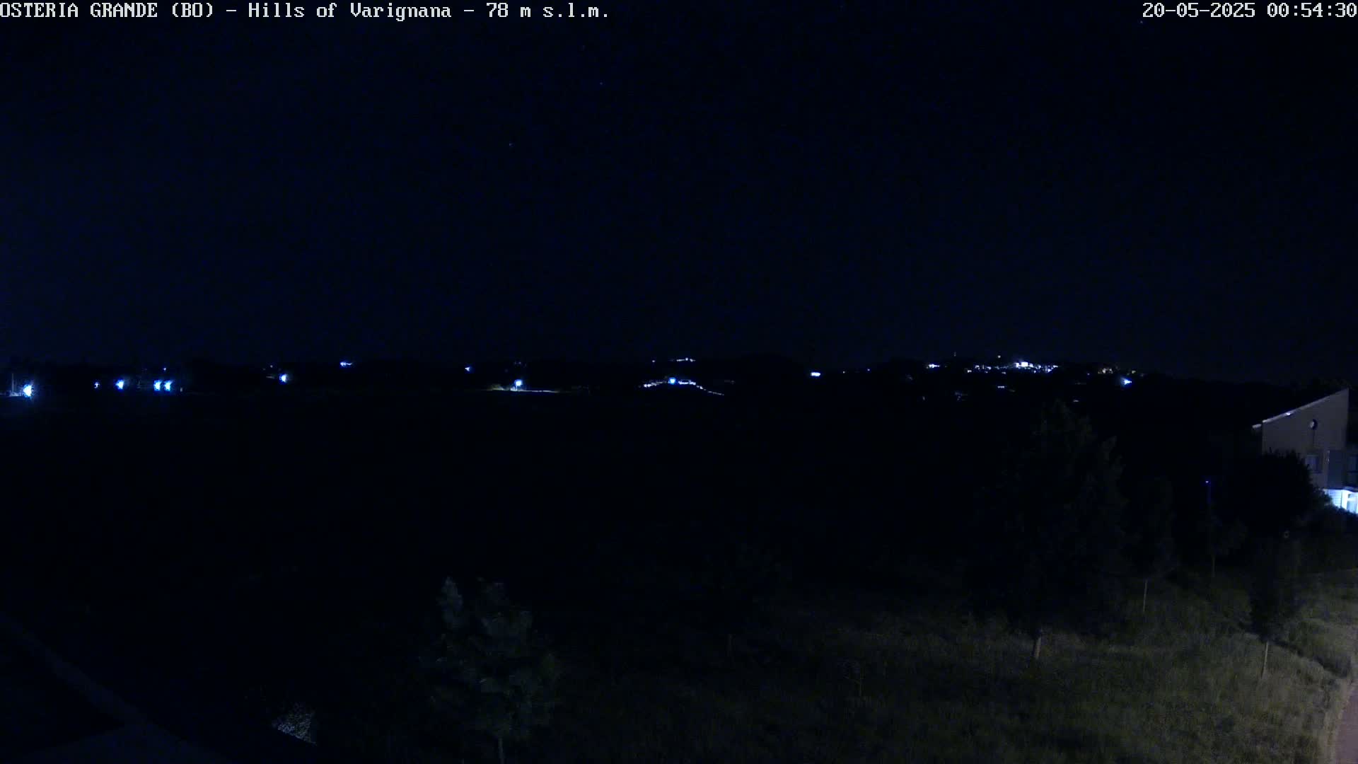 A nighttime view of dark hills with a few distant lights visible under a clear, dark sky.