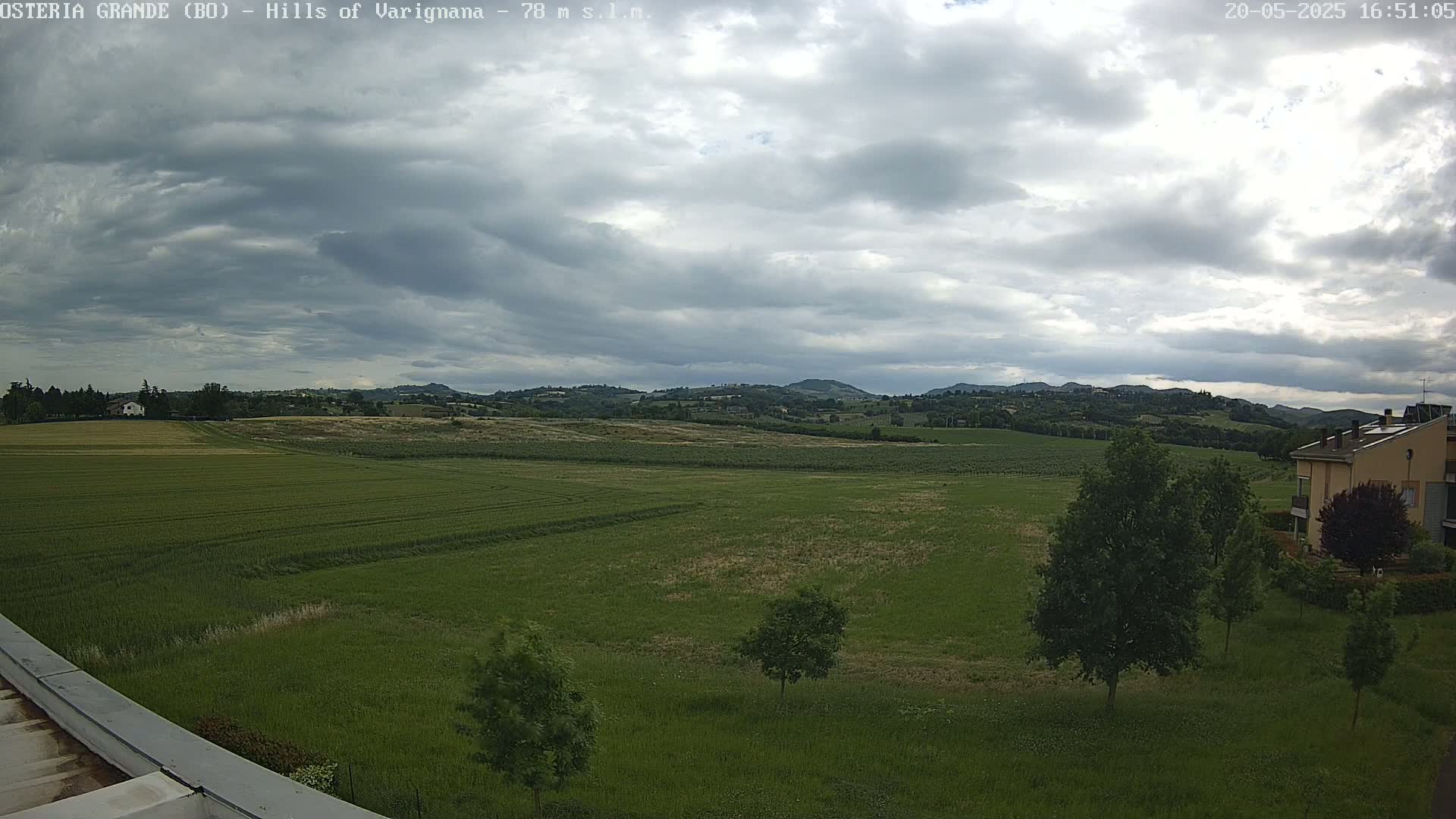 A wide, grassy field stretches to rolling hills under a mostly cloudy sky.