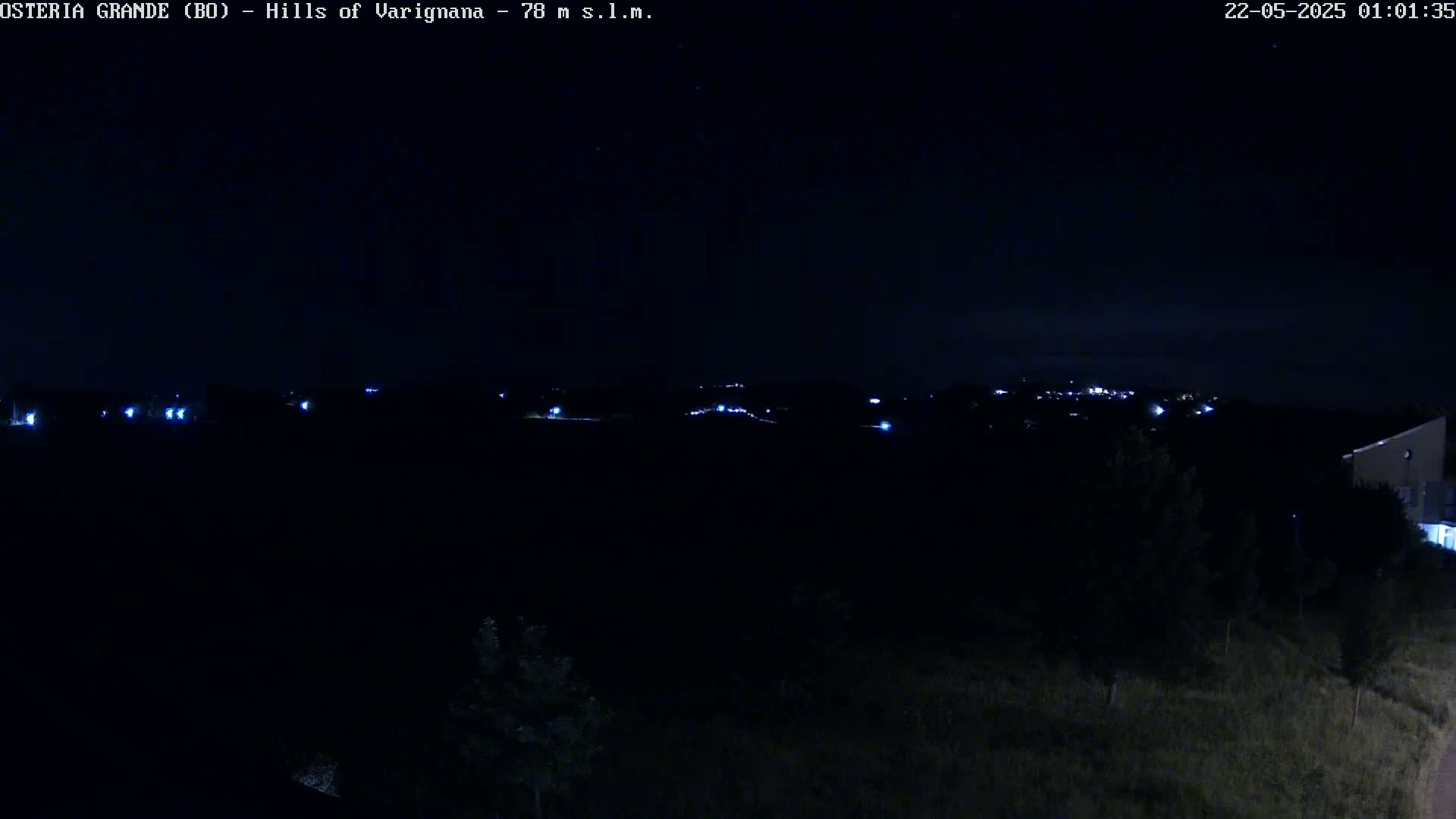 A nighttime, dark landscape view shows a distant line of lights in the hills under a clear, dark sky.