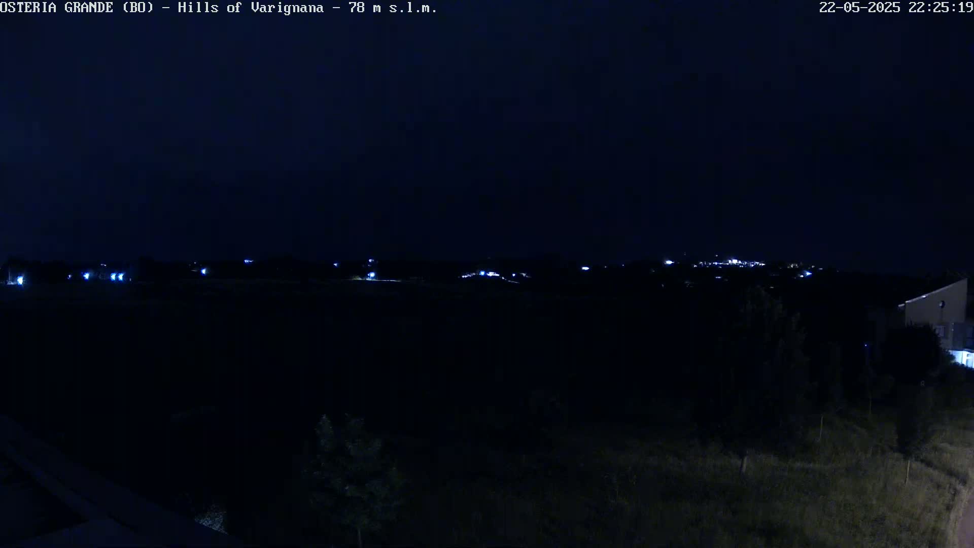 A nighttime long shot of dark hills and a distant town illuminated by faint lights under a clear, dark sky.