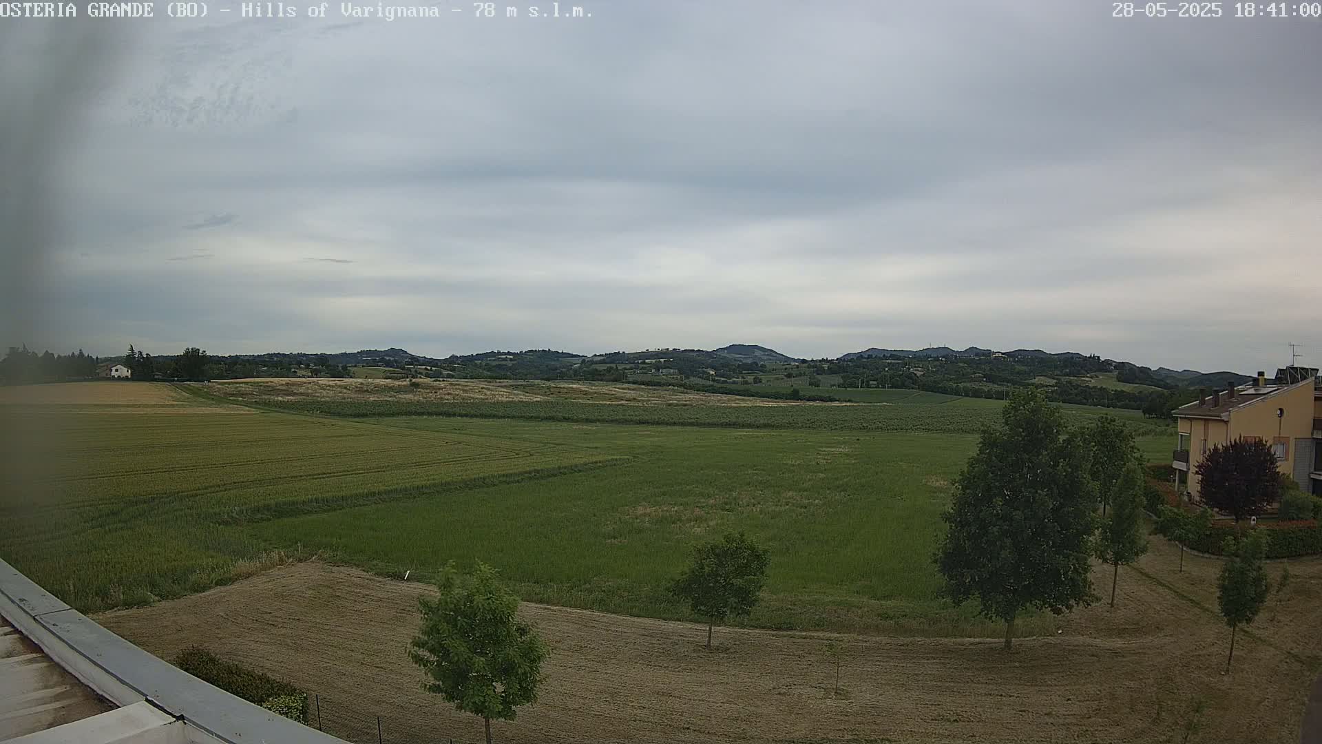 A wide, flat expanse of green and brown farmland stretches toward rolling hills under a cloudy sky.