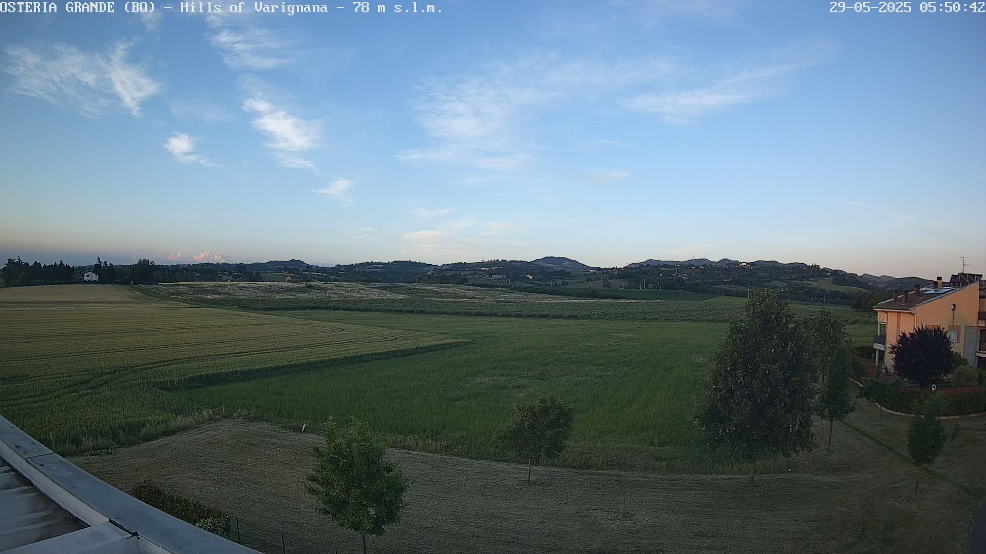 A wide, expansive view of rolling green fields and distant hills under a mostly clear, light-blue sky.