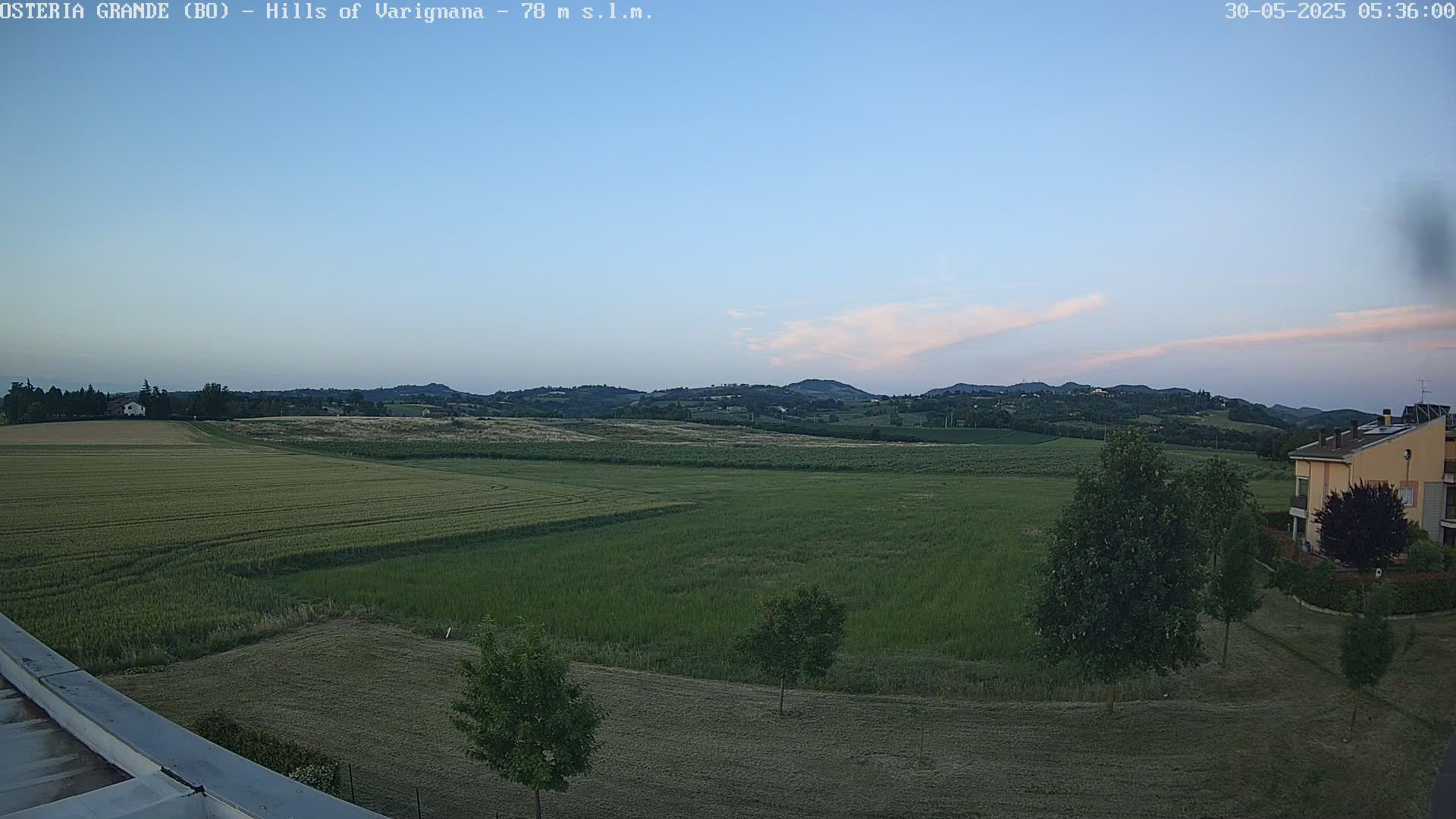 Under a clear, twilight sky, a vast expanse of verdant fields stretches towards rolling hills in the distance.