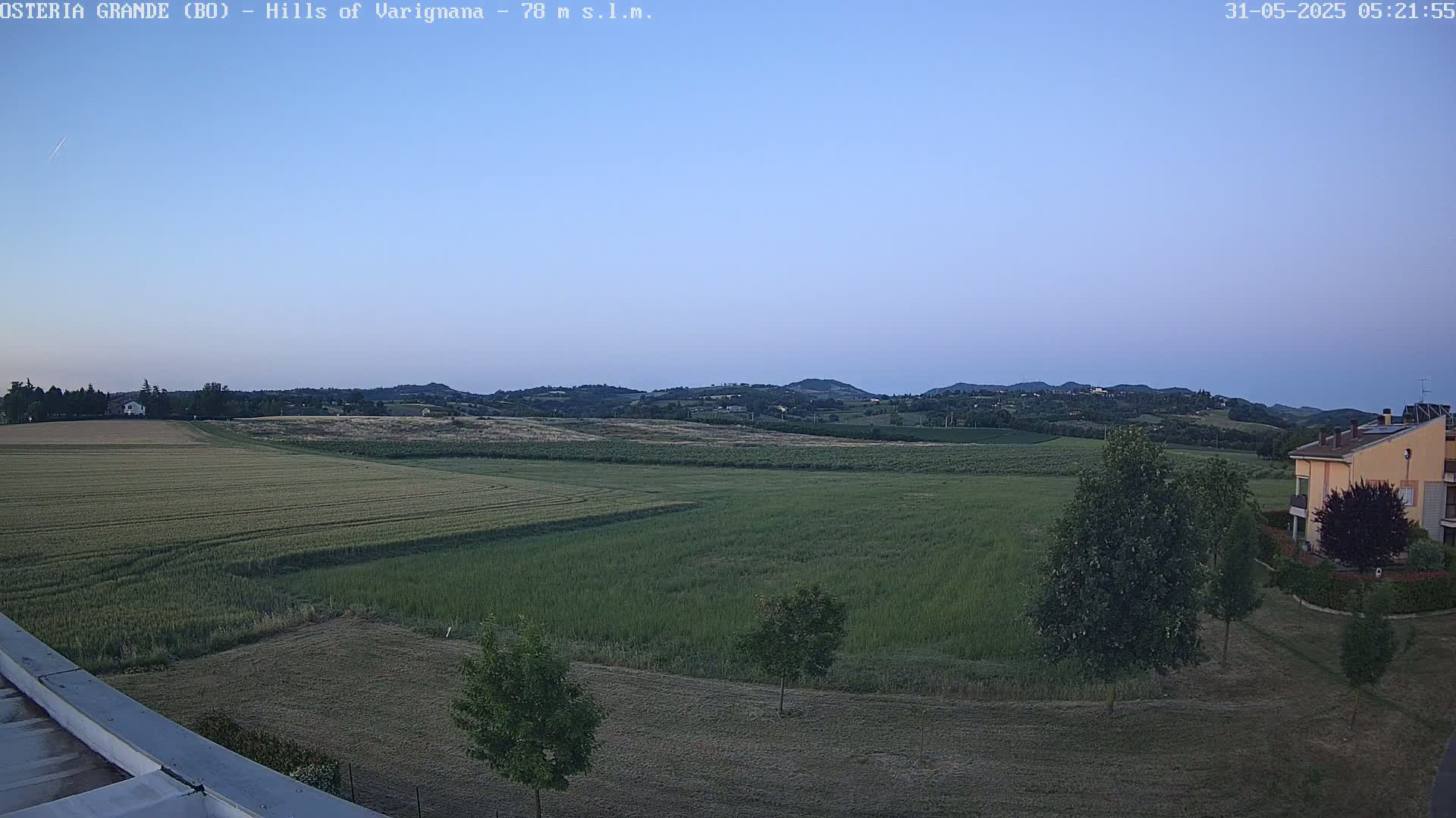 A wide, flat field of crops stretches out to a line of rolling hills under a clear twilight sky.