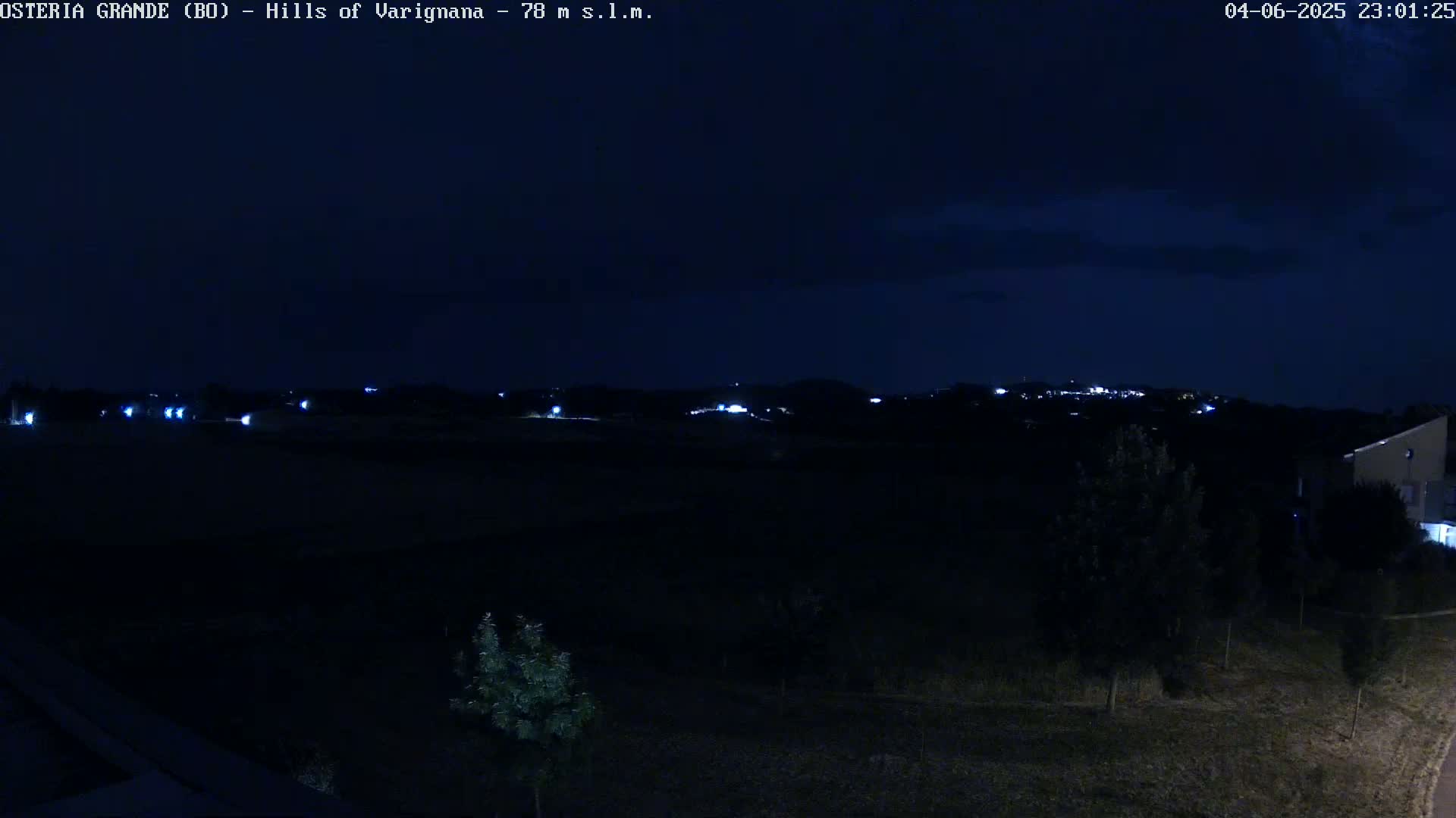 A nighttime, dark view of distant lights in a town or village nestled in the hills under a mostly clear, dark sky.