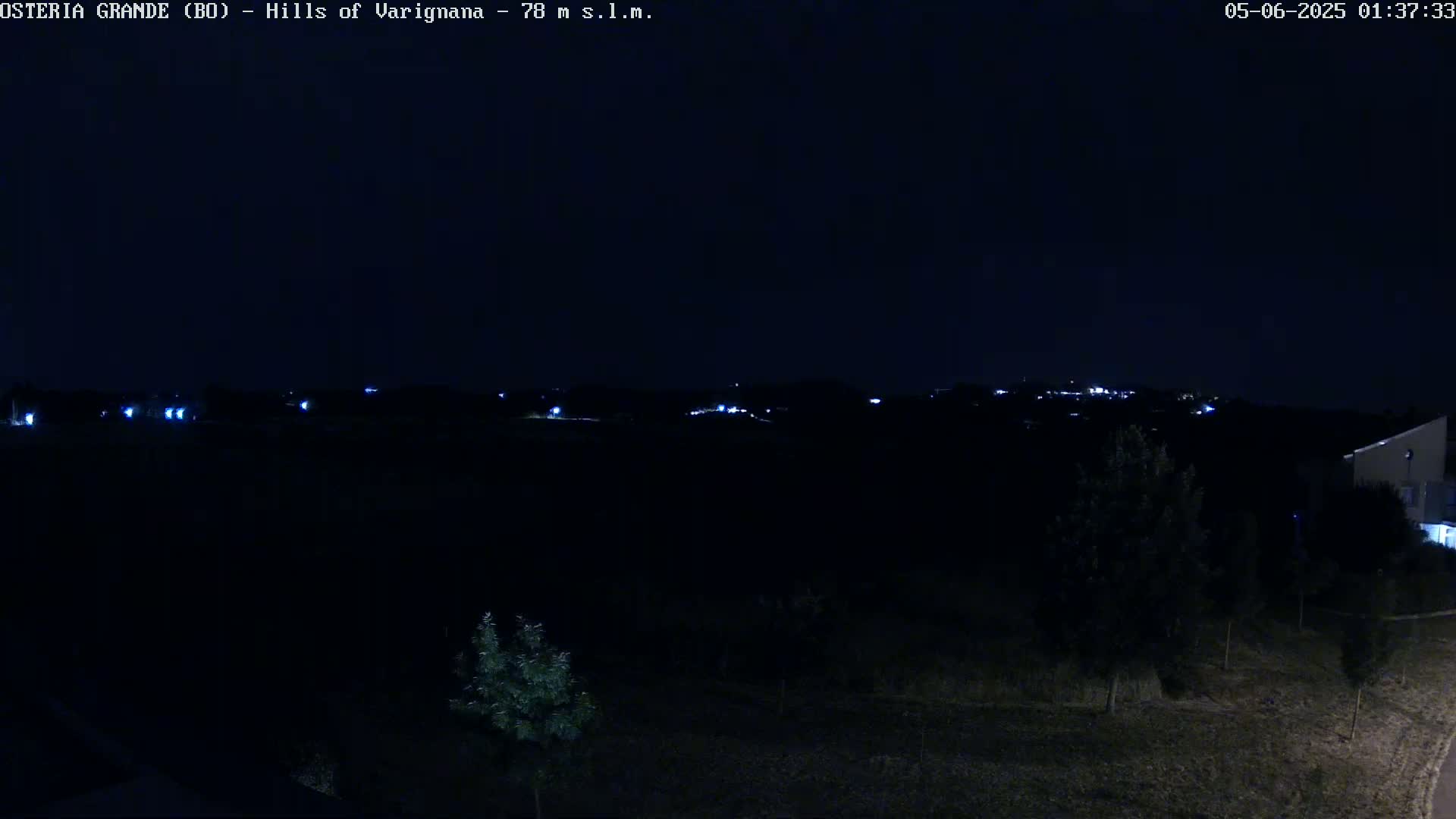 A dark nighttime landscape shows a distant line of faintly lit buildings on a hill under a clear, dark sky.