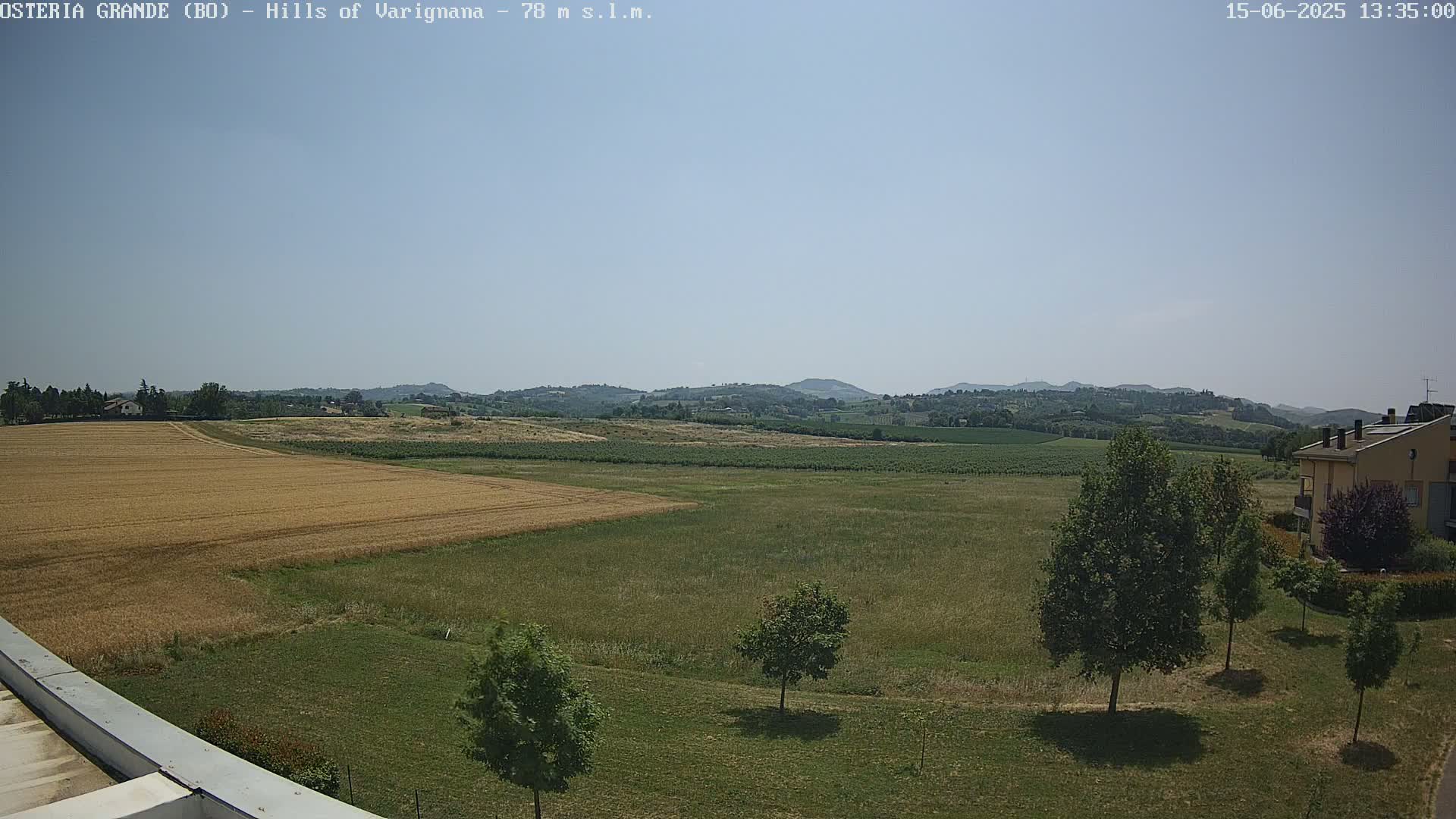 A sunny day reveals a wide expanse of farmland, with golden wheat fields and rolling green hills in the distance.