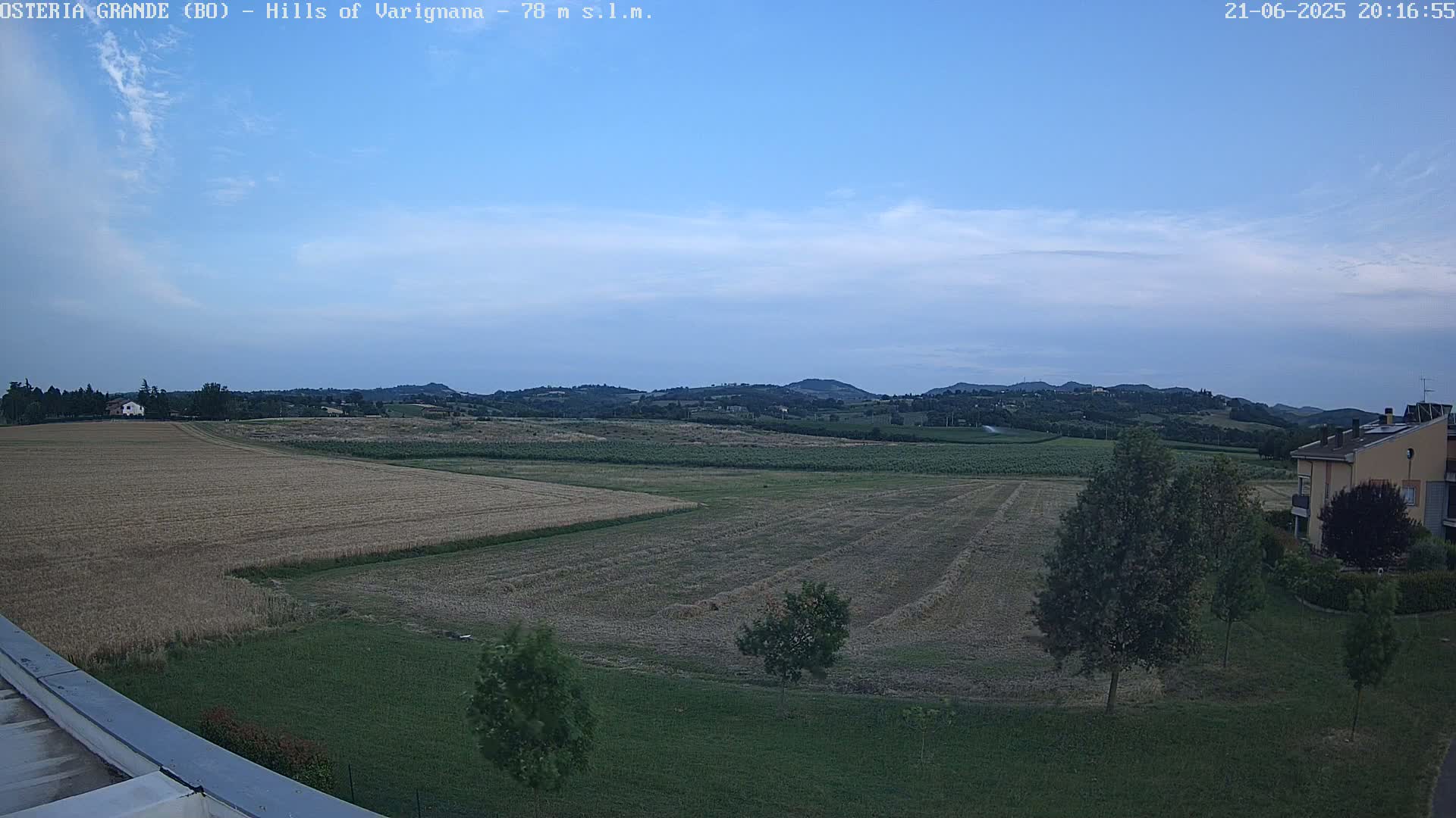 A wide, flat expanse of harvested fields stretches towards rolling hills under a twilight sky.