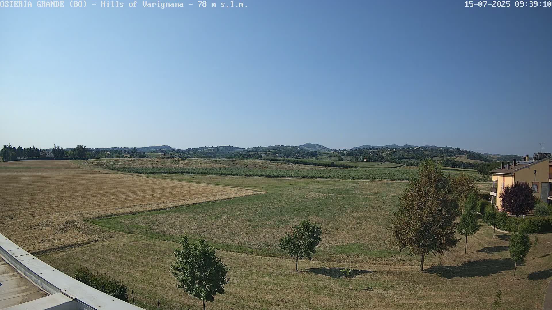A clear, sunny day reveals rolling hills of farmland, interspersed with trees and a residential building in the distance.