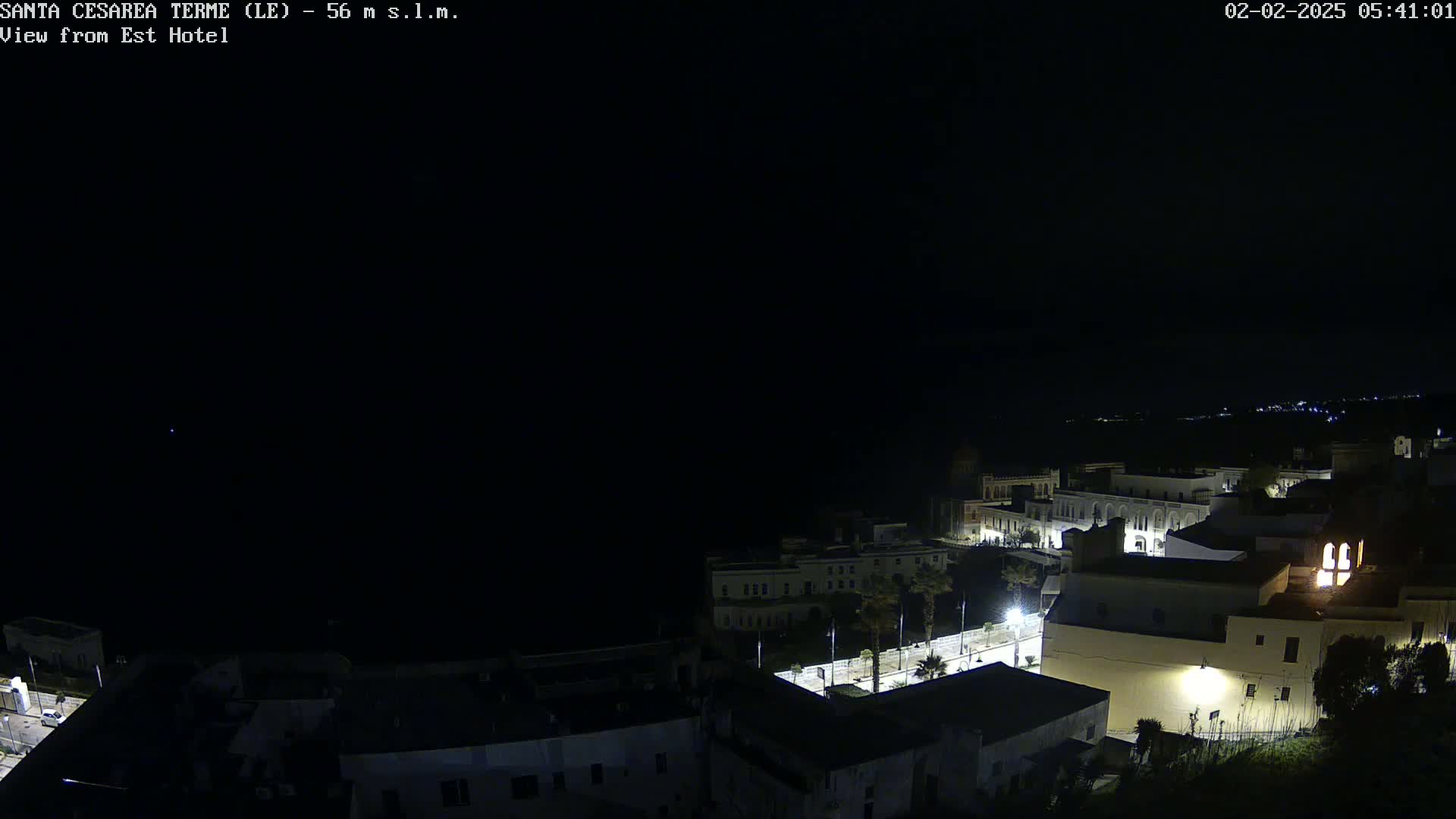 A nighttime, high-angle view of a coastal town with buildings illuminated against a dark sky and sea.