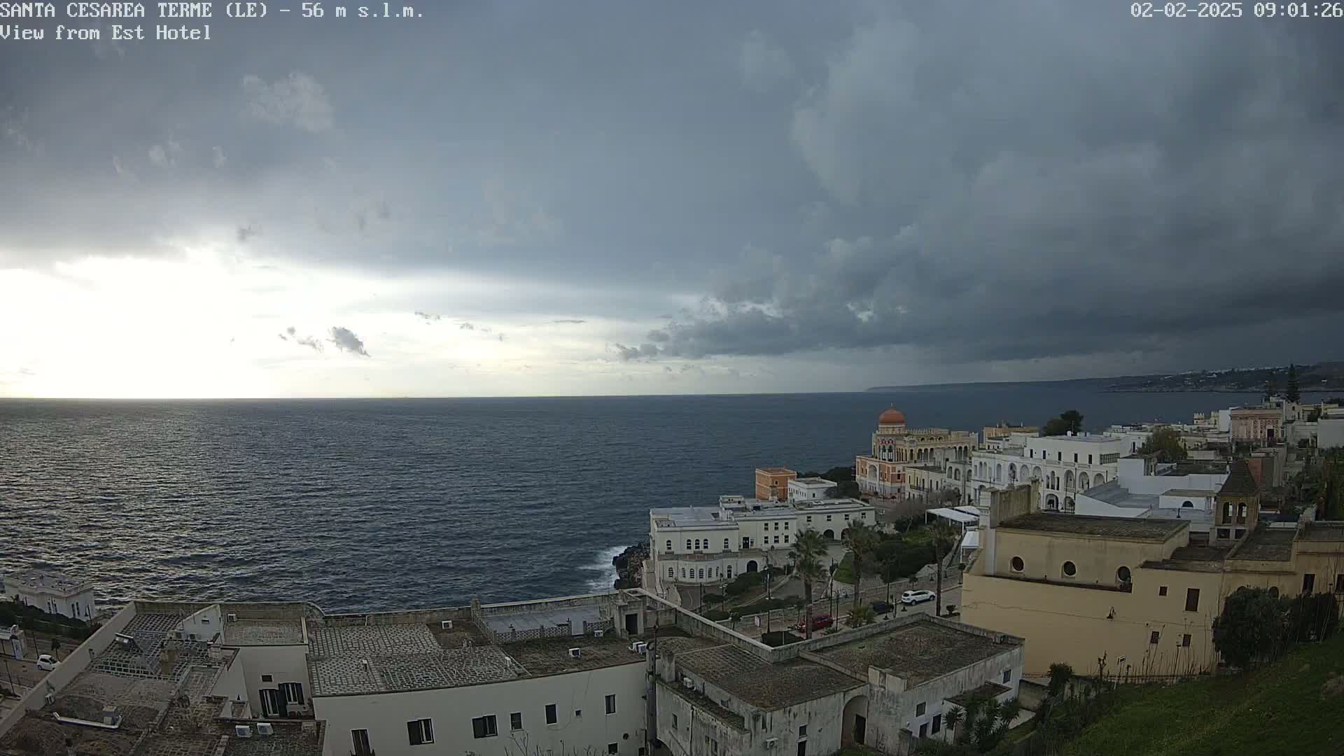 A coastal town with white buildings overlooks a dark, choppy sea under a mostly cloudy sky.
