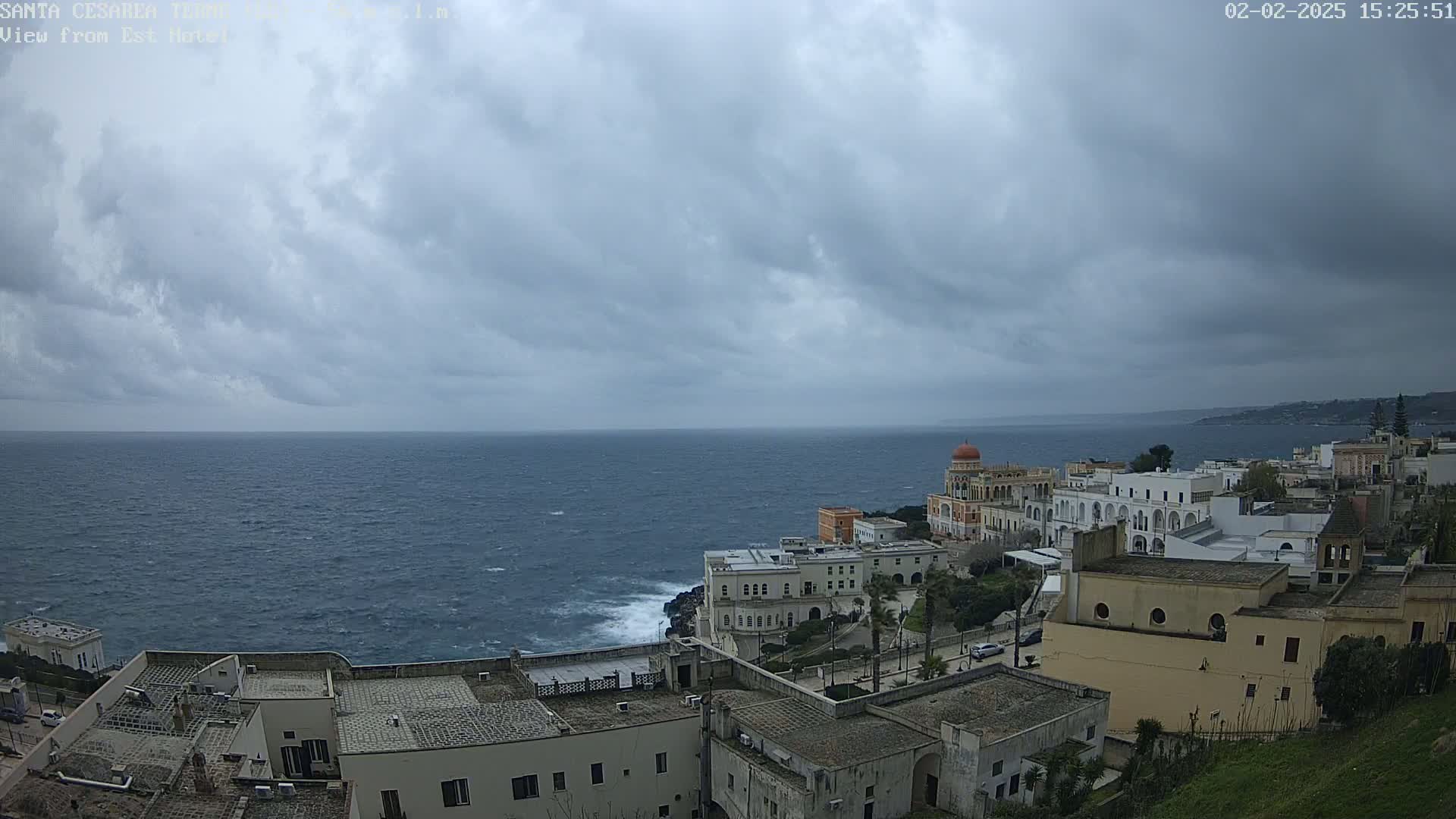 A coastal town with white buildings overlooks a choppy sea under a cloudy sky.