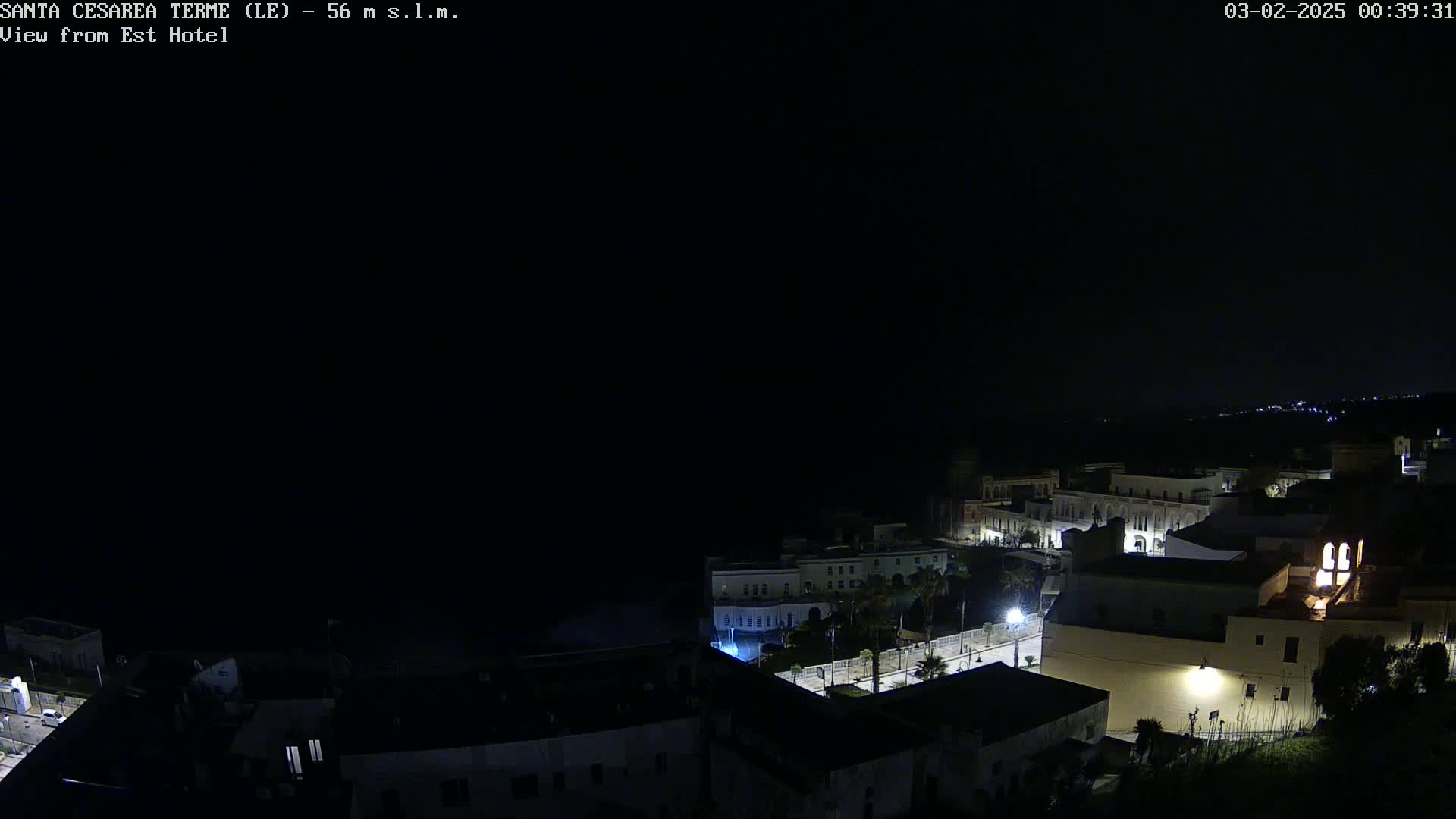 A nighttime view of a coastal town shows buildings illuminated by streetlights under a clear, dark sky.