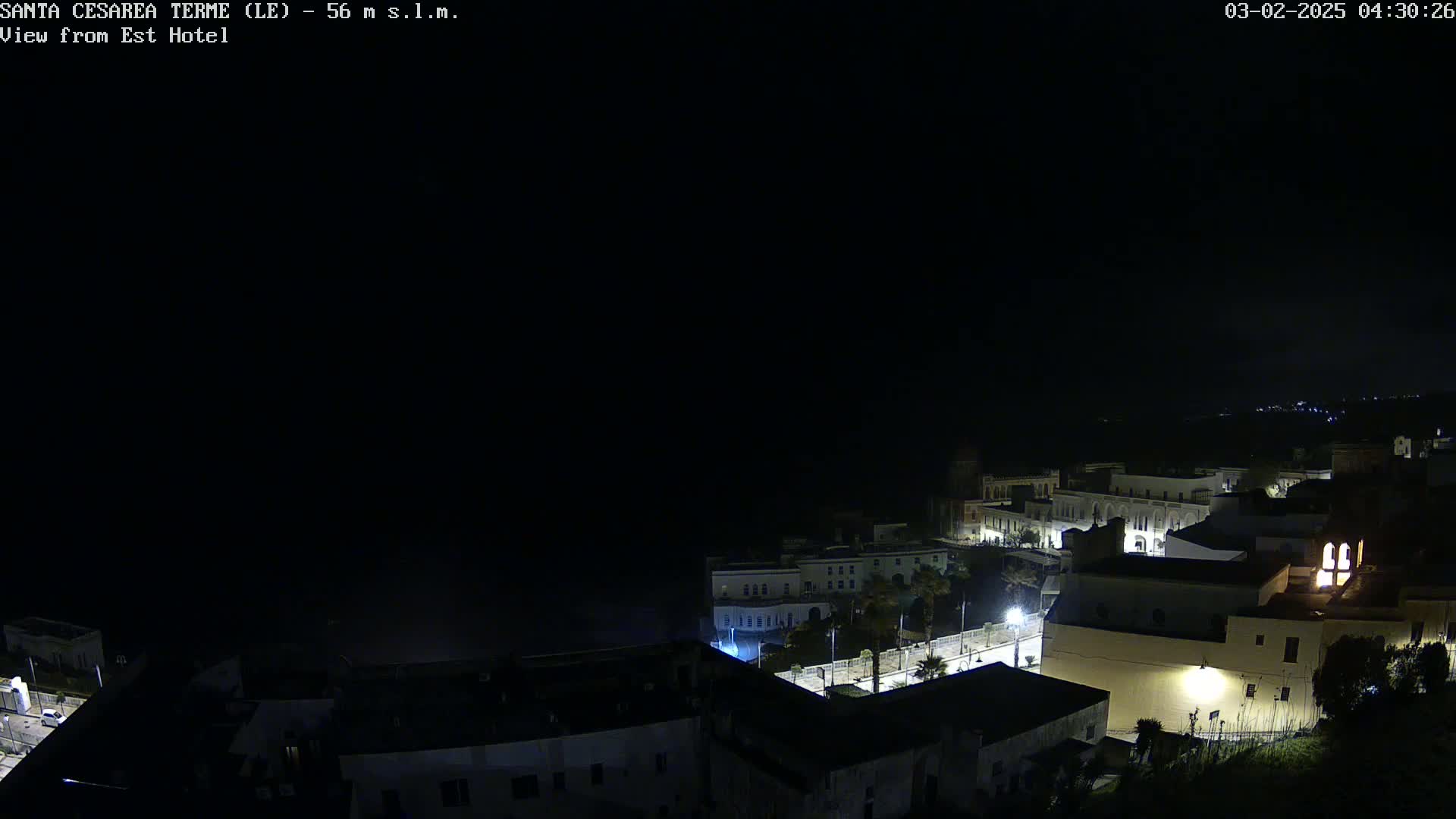 A nighttime, high-angle view of a coastal town with dimly lit buildings under a dark sky.