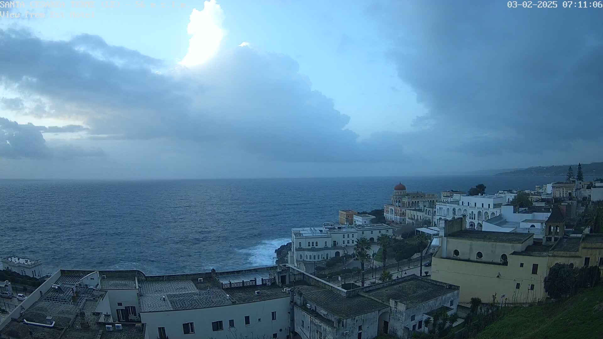 A coastal town with white buildings is visible under a partly cloudy sky, with a choppy sea extending to the horizon.