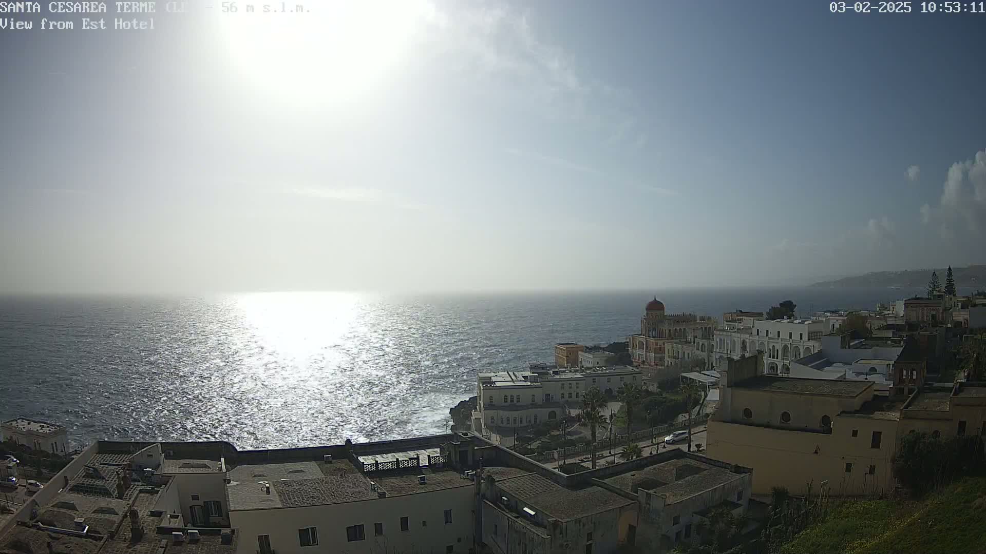 A bright, sunny day overlooks a coastal town with buildings cascading down to a sparkling sea.