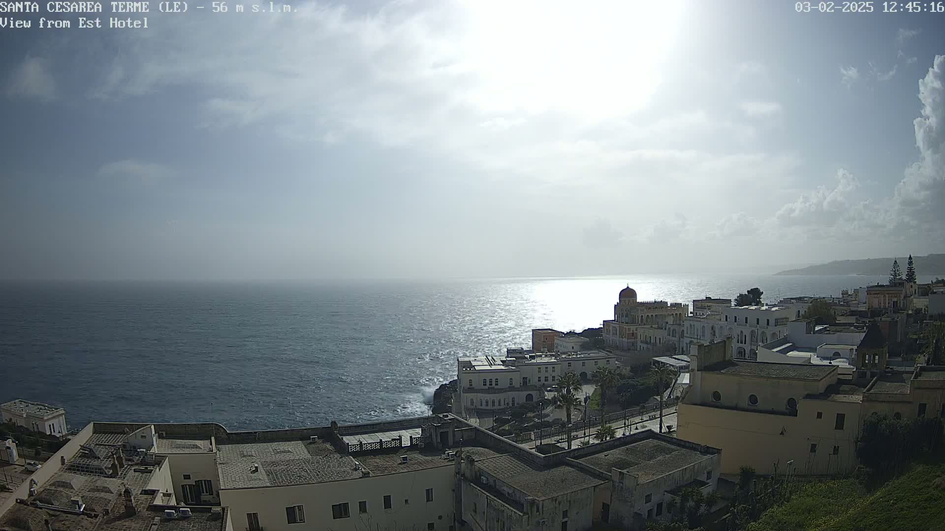 A partly cloudy day reveals a coastal town nestled on a cliff overlooking a wavy sea.