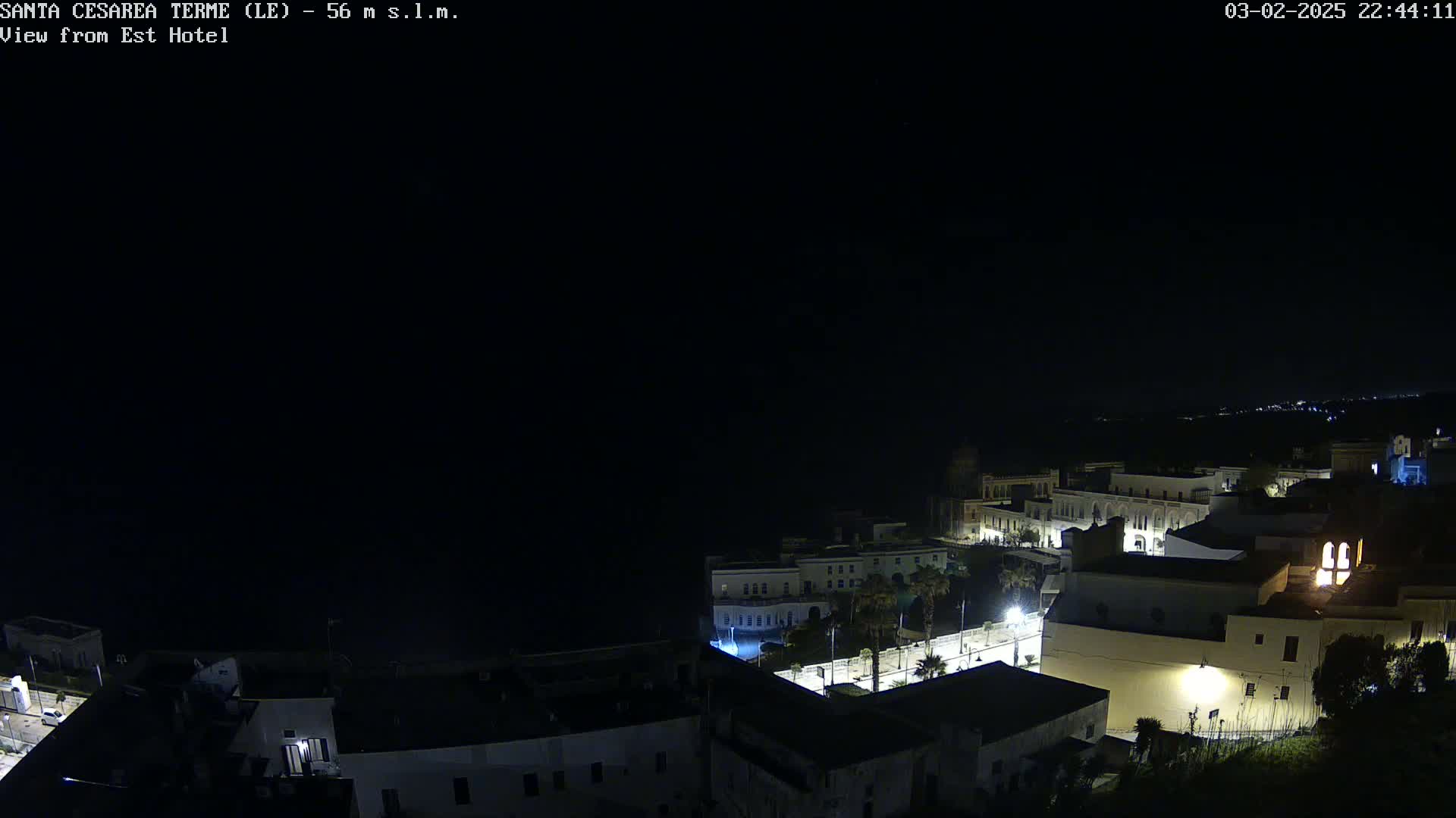 A nighttime, aerial view of a coastal town with buildings illuminated against a dark sky.