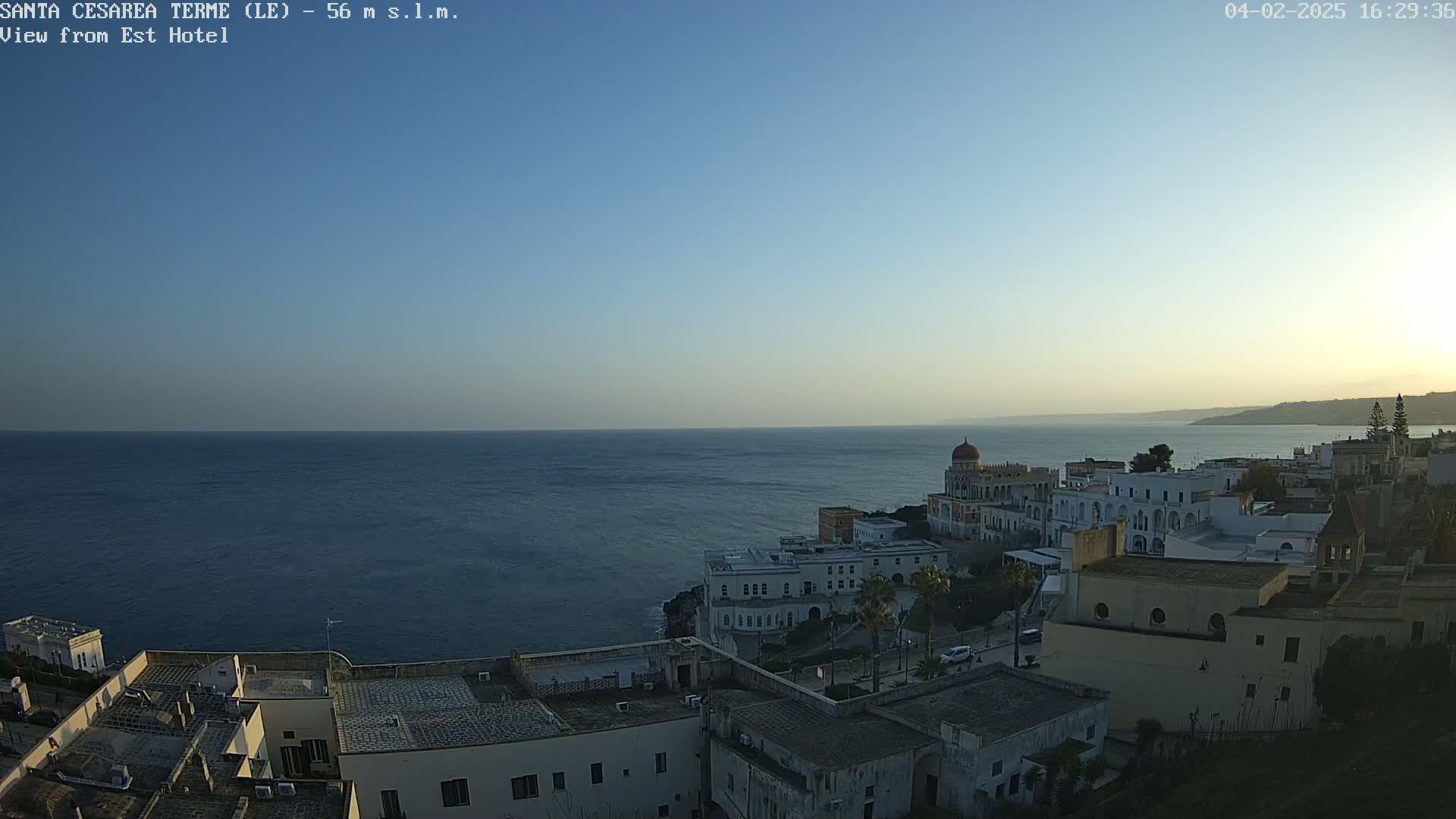 A coastal town with white buildings and a calm, dark-blue sea under a clear, light-blue sky.