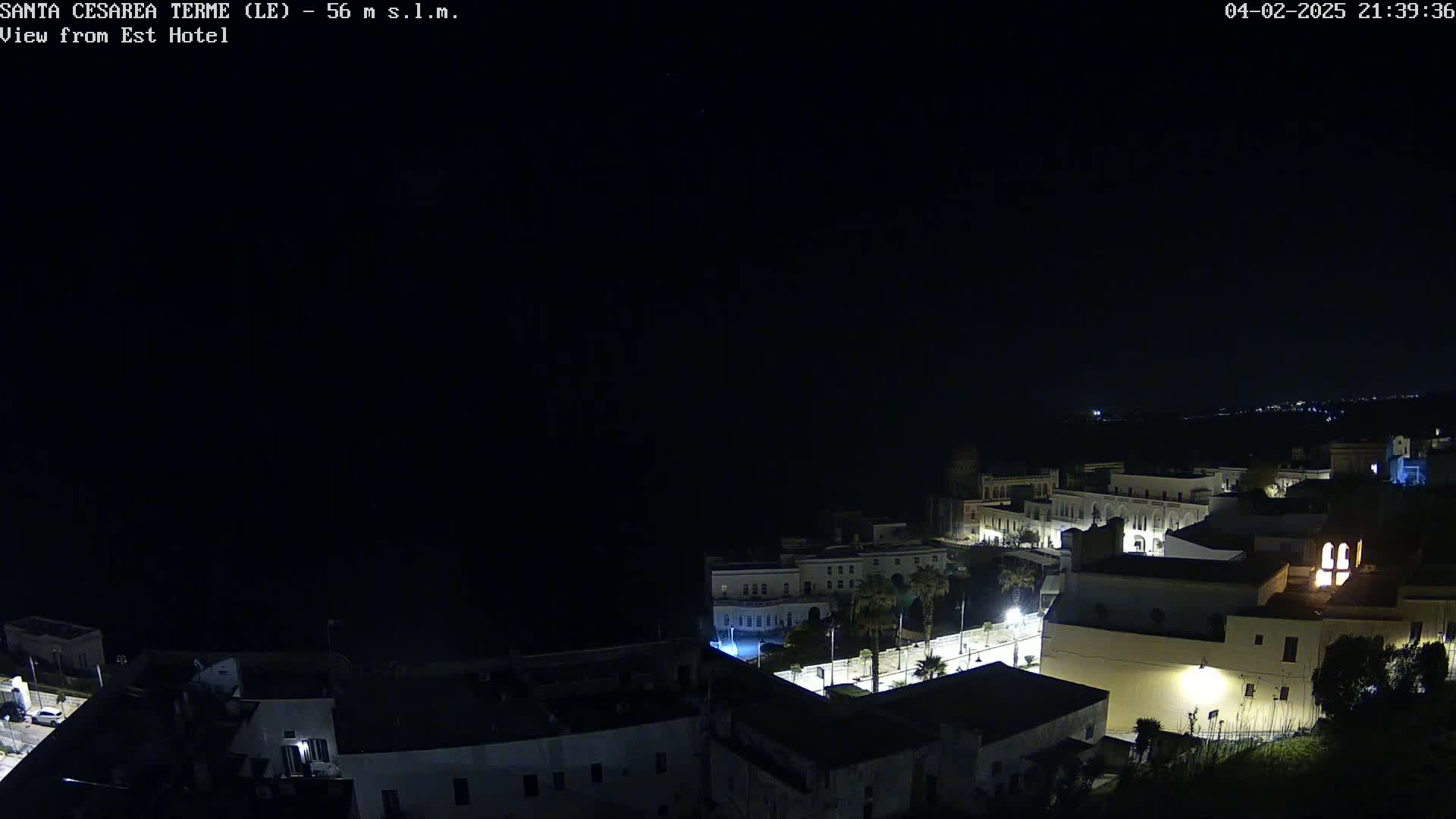 A nighttime, aerial view of a coastal town with dimly lit buildings under a clear, dark sky.