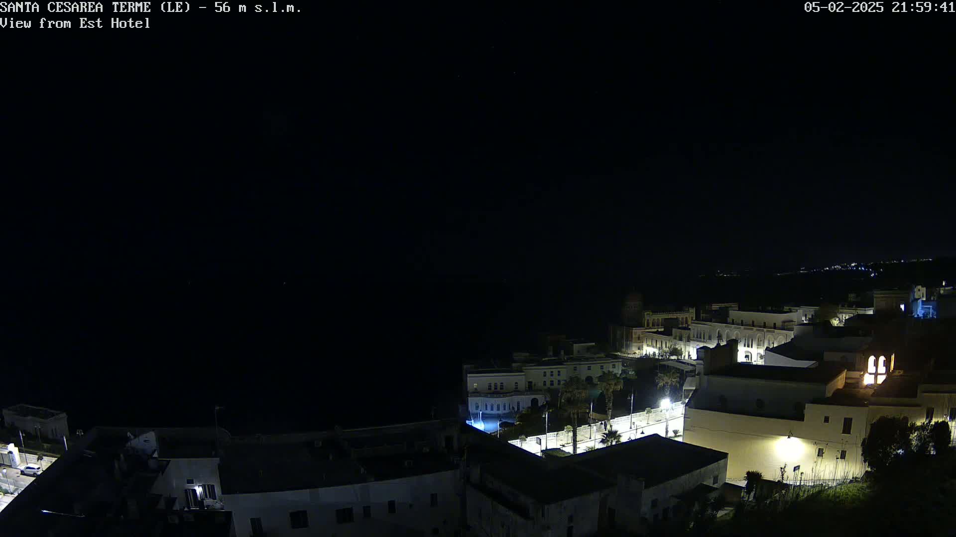 A nighttime, aerial view of a coastal town with dimly lit buildings and a dark ocean.
