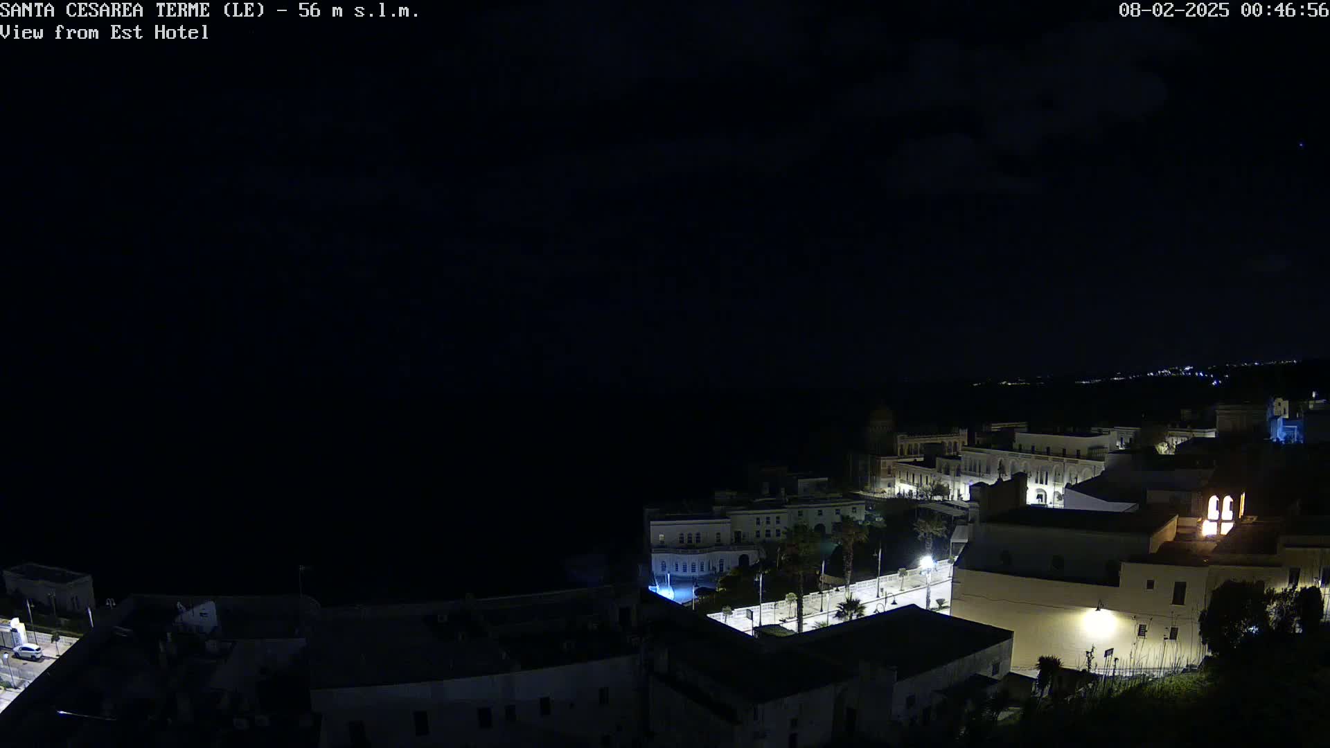 A nighttime, high-angle view of a coastal town, sparsely lit, with the dark ocean visible in the background.