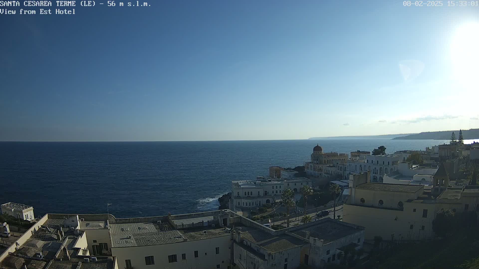 A coastal town with white buildings stretches along a dark blue sea under a clear, bright sky.