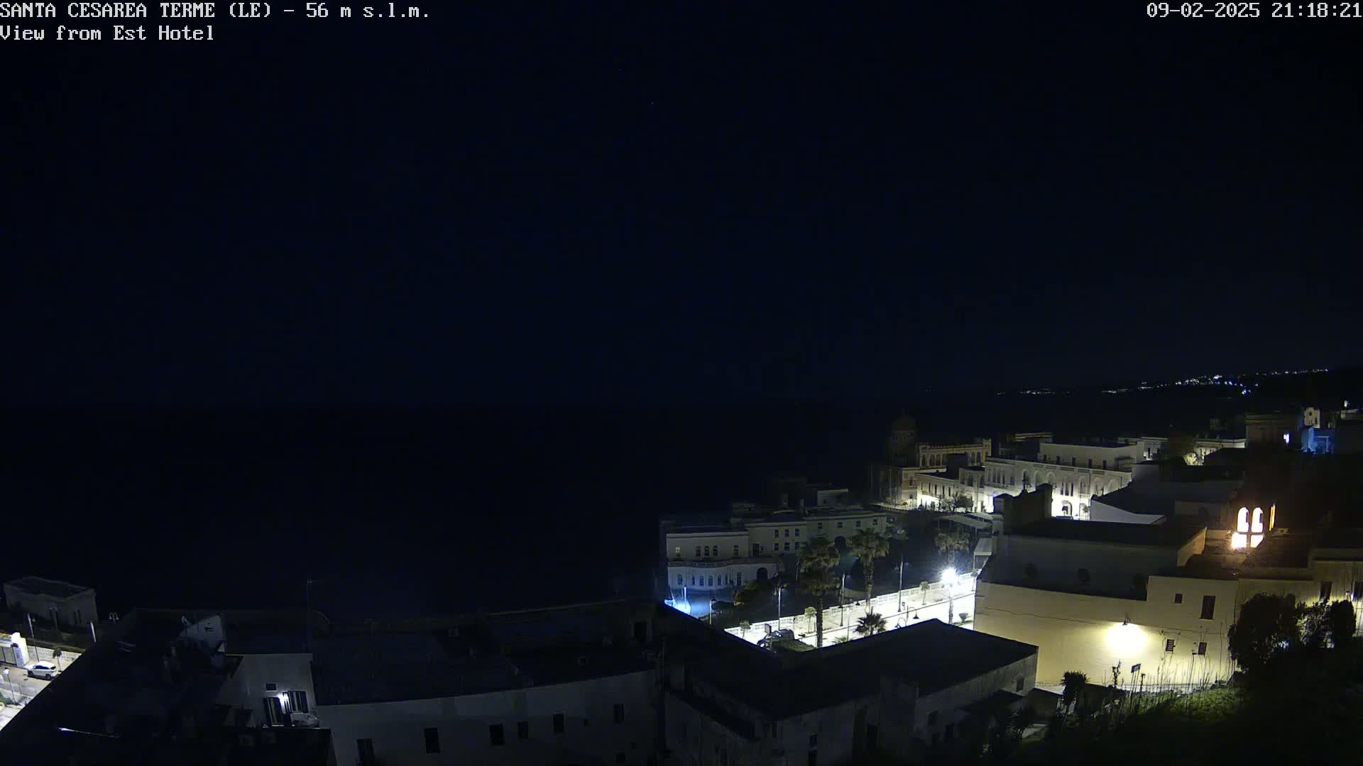 A nighttime view of a coastal town, with dark water visible in the distance under a clear, dark sky.