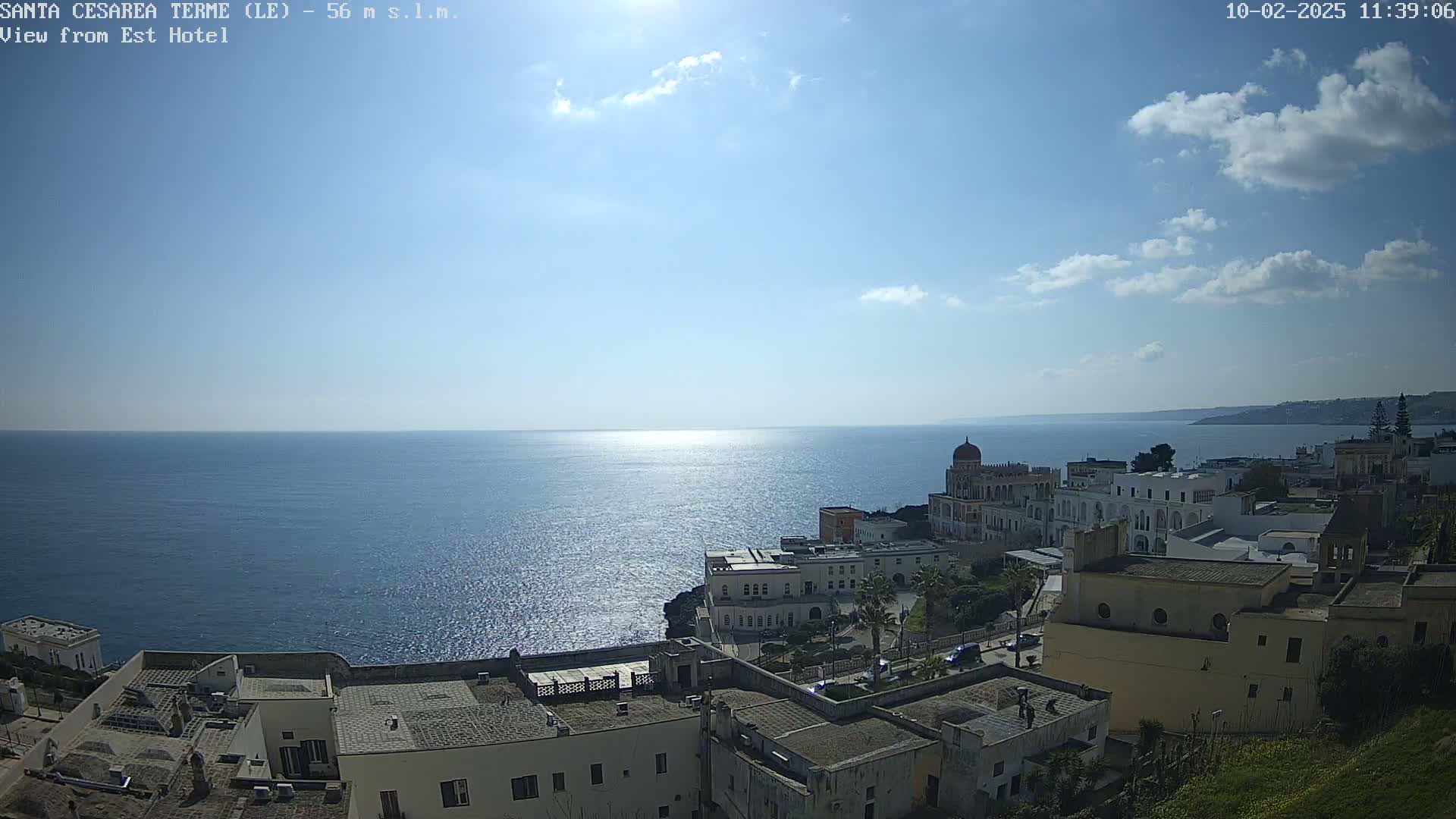 A sunny day with a few clouds reveals a coastal town overlooking a calm sea.