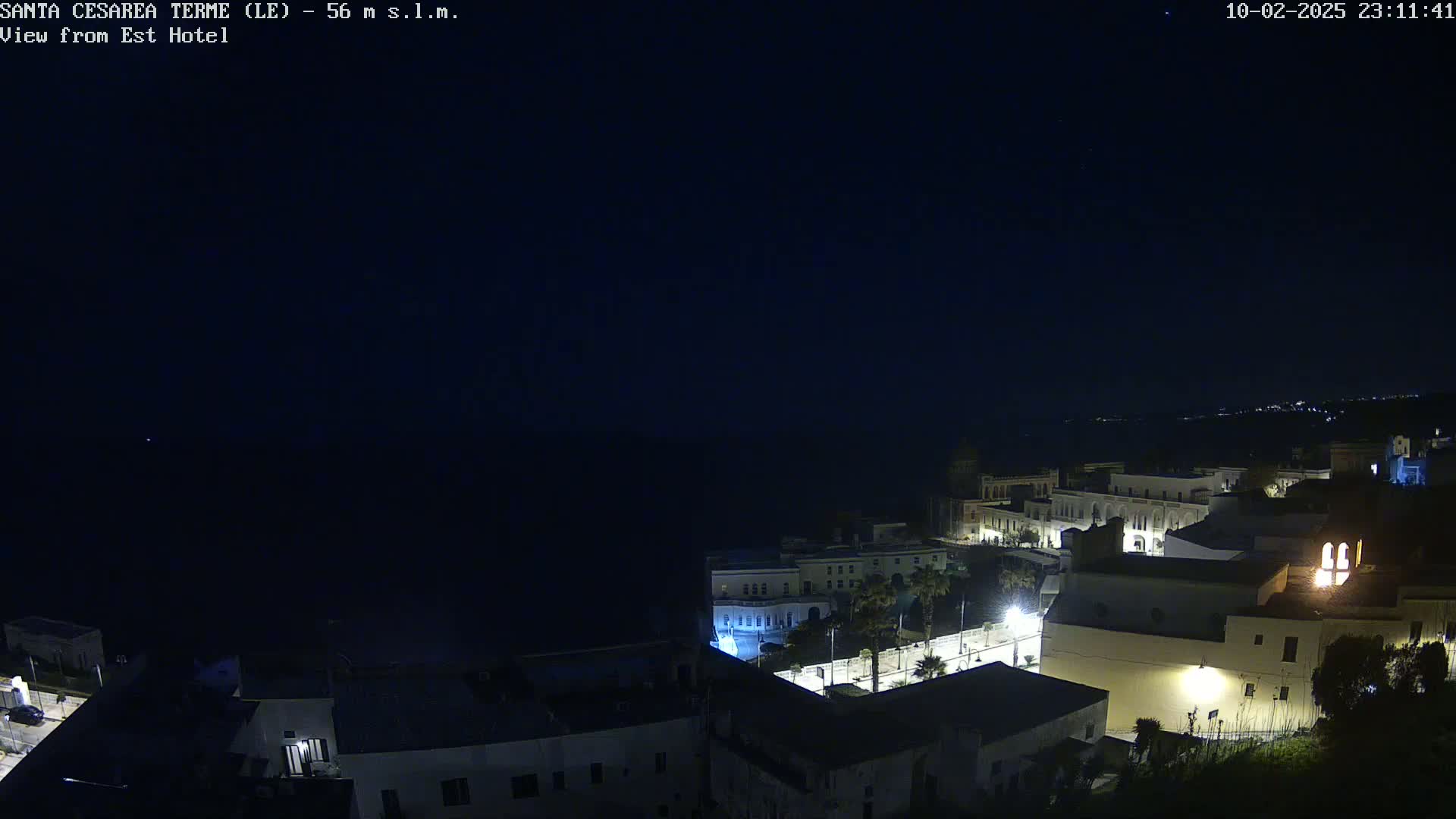 A nighttime, high-angle view of a coastal town with buildings illuminated against a dark sky.