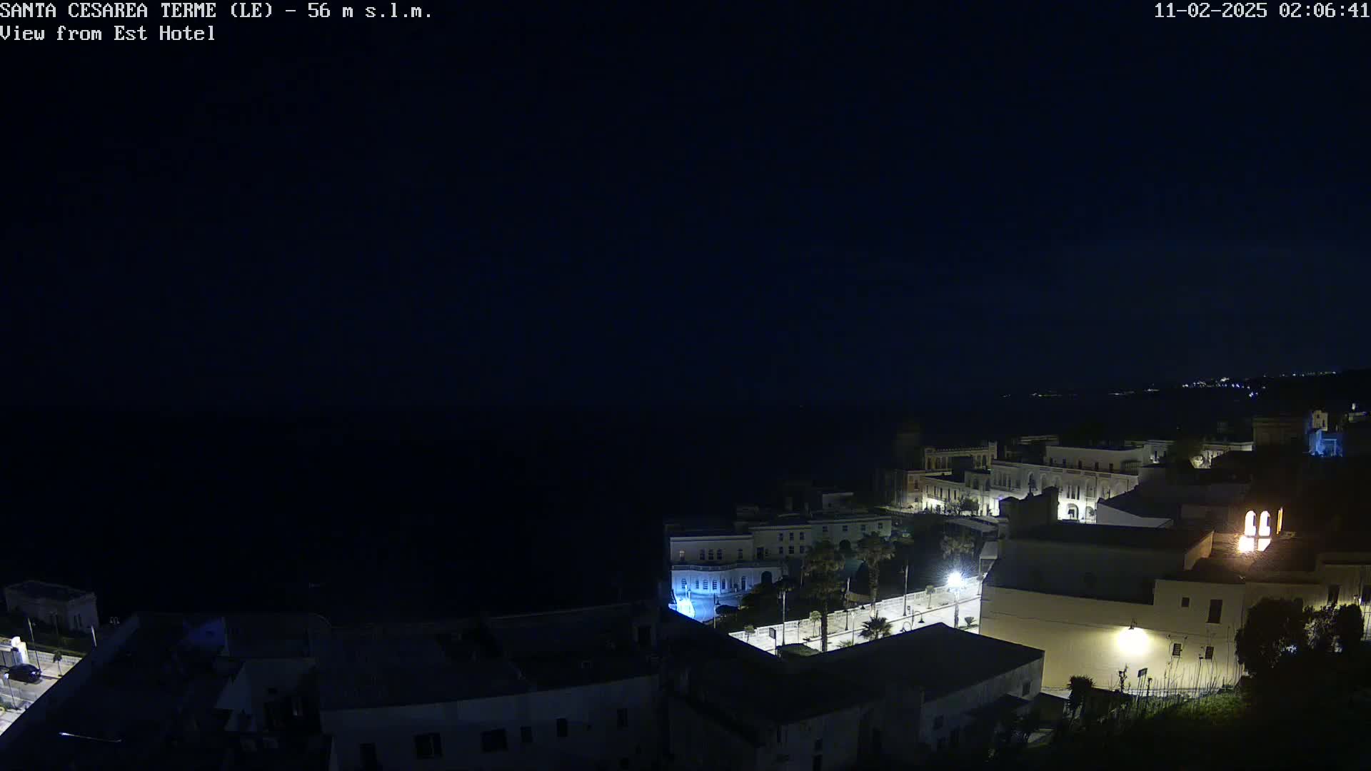 A nighttime, high-angle view of a coastal town with buildings illuminated against a dark sea and sky.