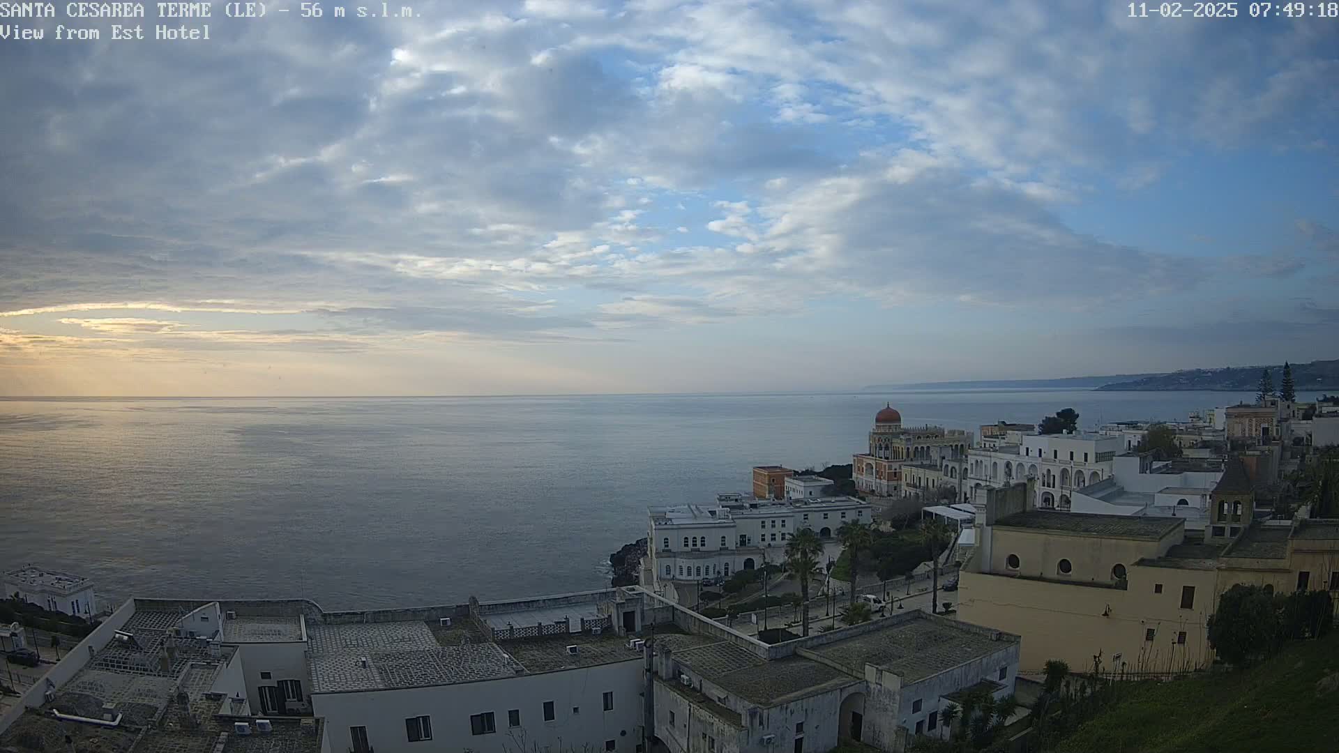 A coastal town with white buildings and a calm sea under a partly cloudy sky.