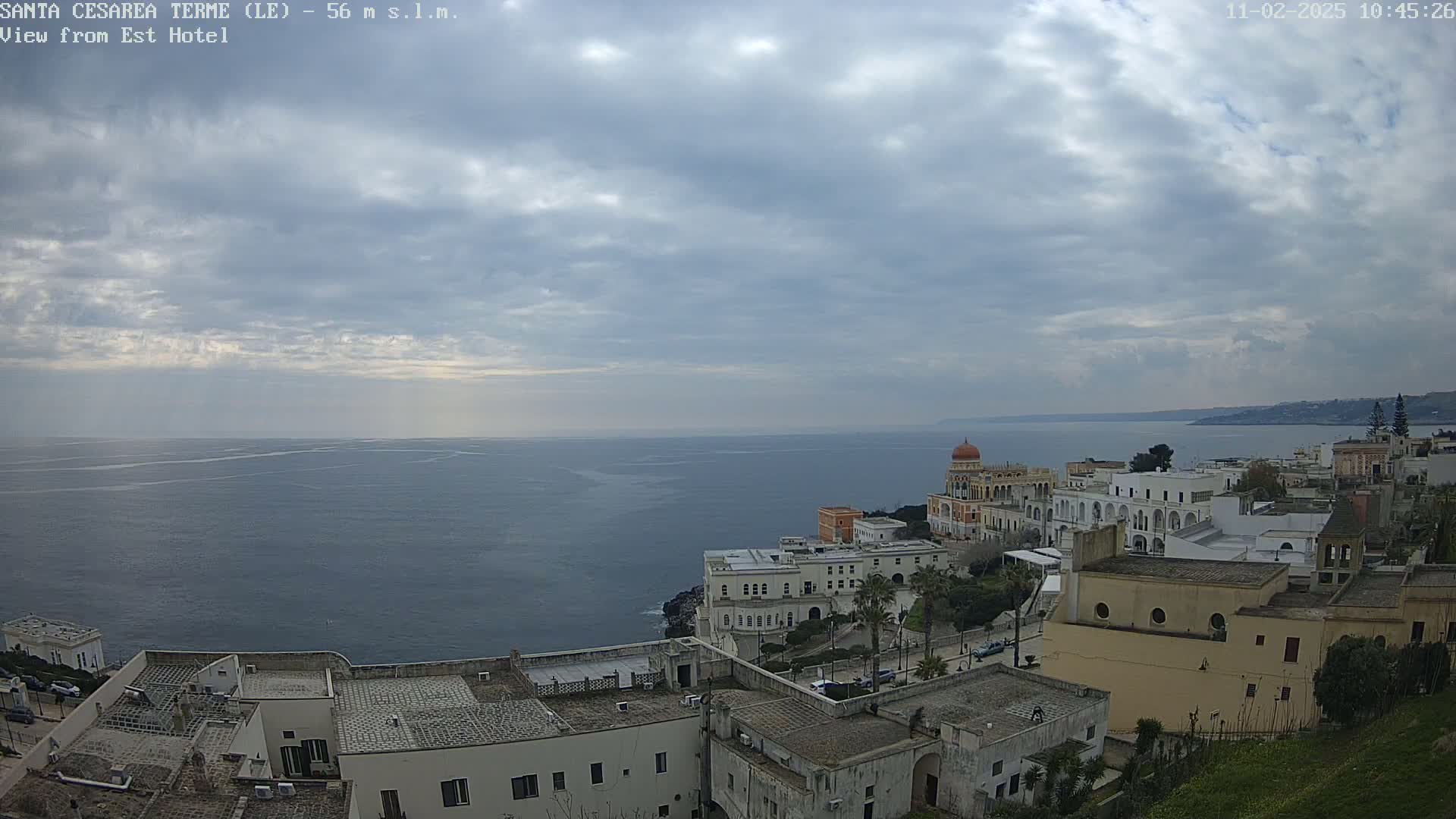 A coastal town with white buildings and a calm sea under a cloudy sky.