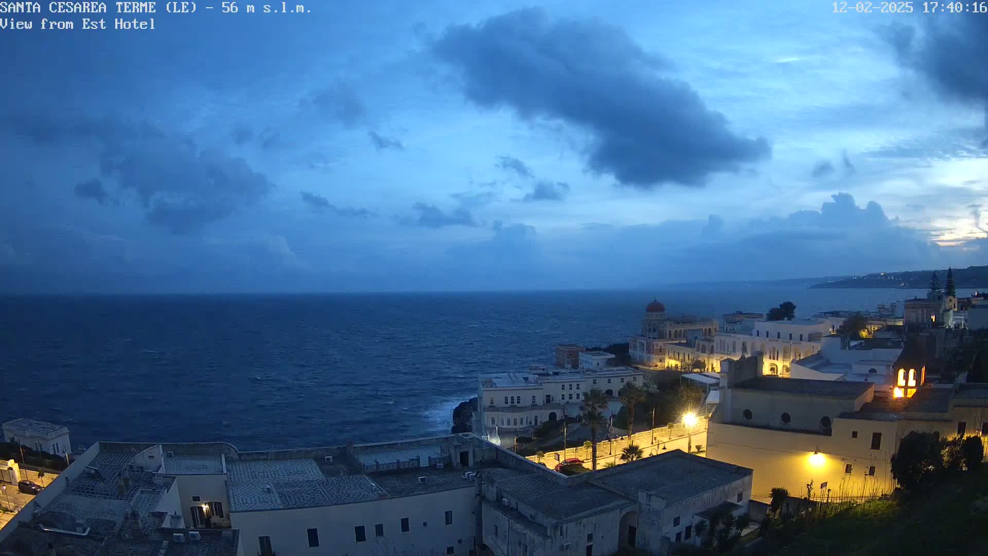 A coastal town at dusk, with a dark blue, somewhat cloudy sky and a choppy sea.