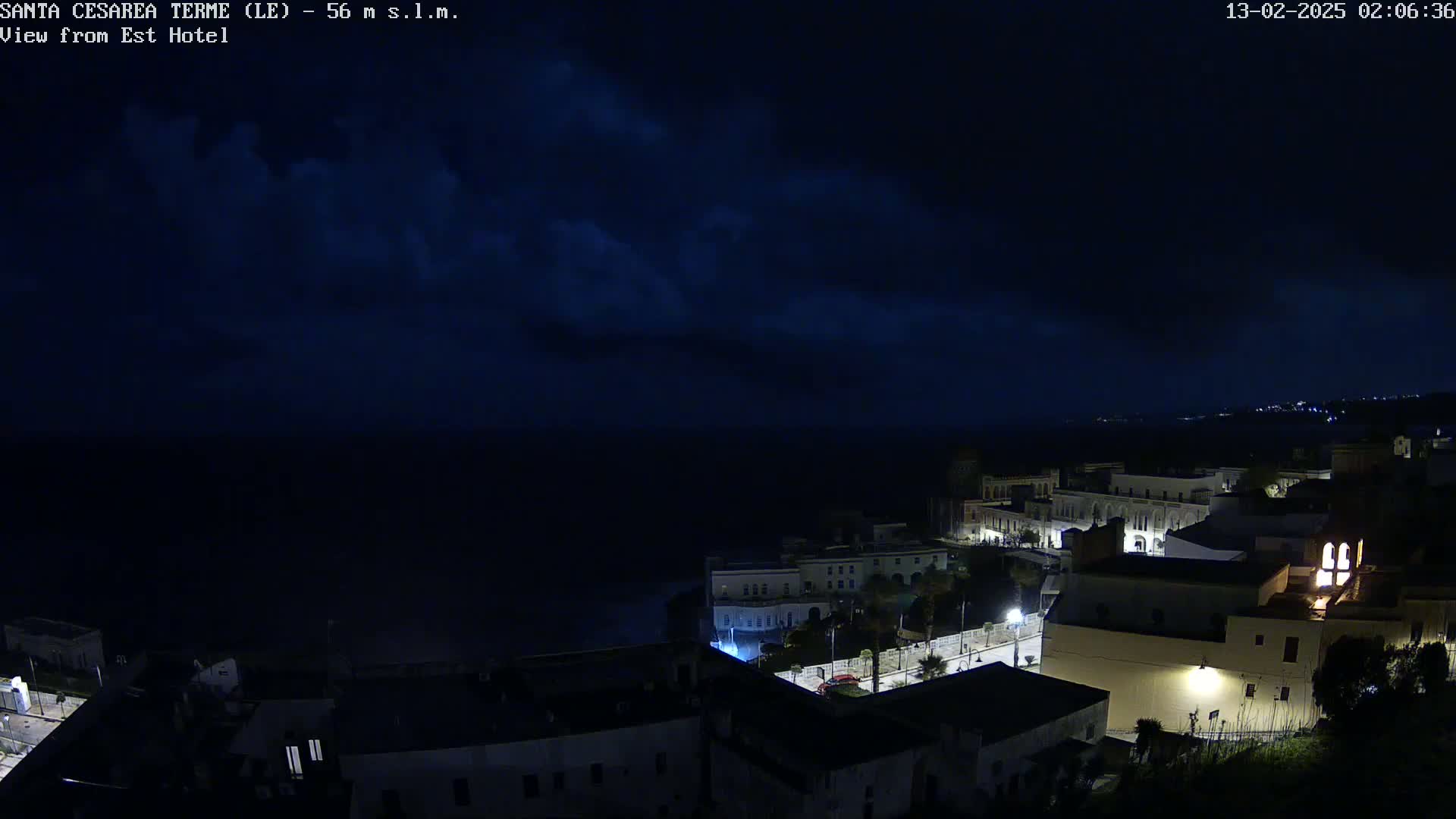 A nighttime coastal town with dimly lit buildings is visible under a dark sky with some clouds.