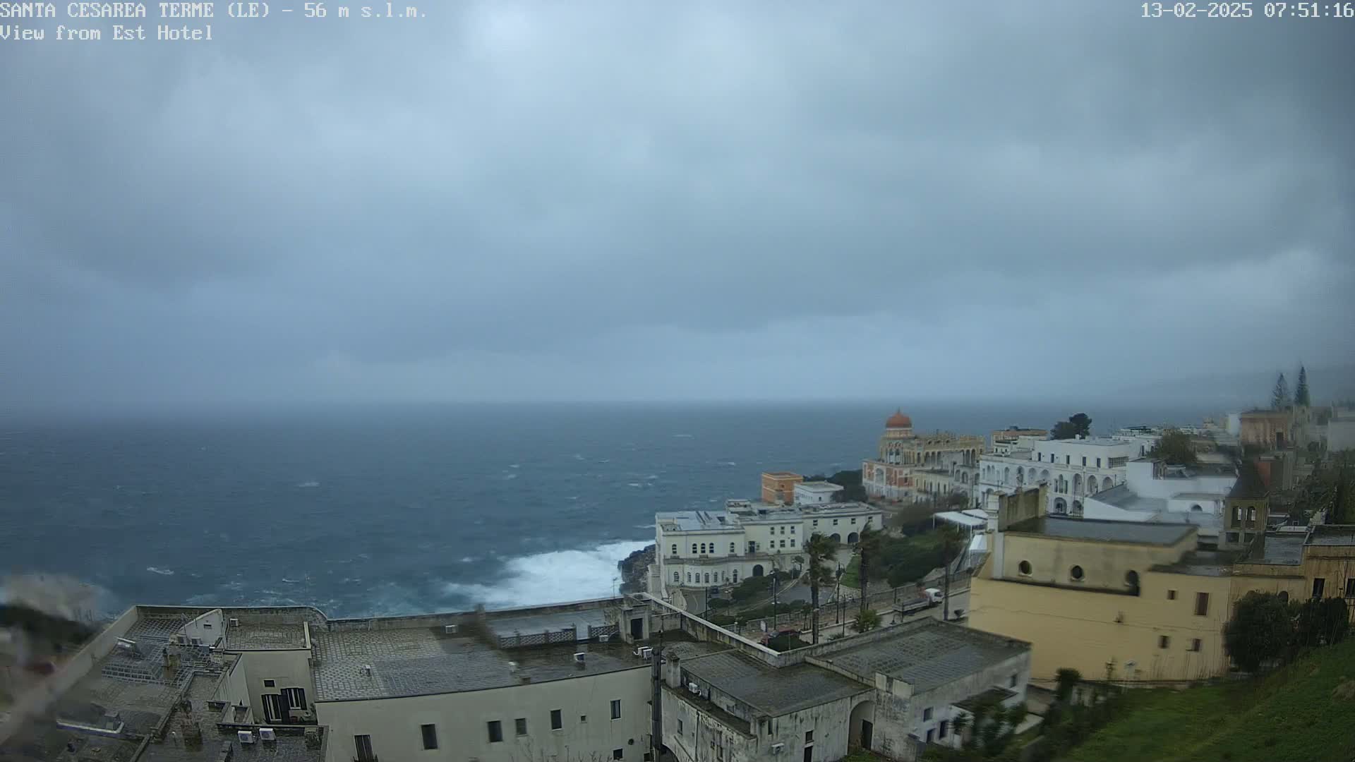 A coastal town with white buildings overlooks a rough, choppy sea under a cloudy, overcast sky.