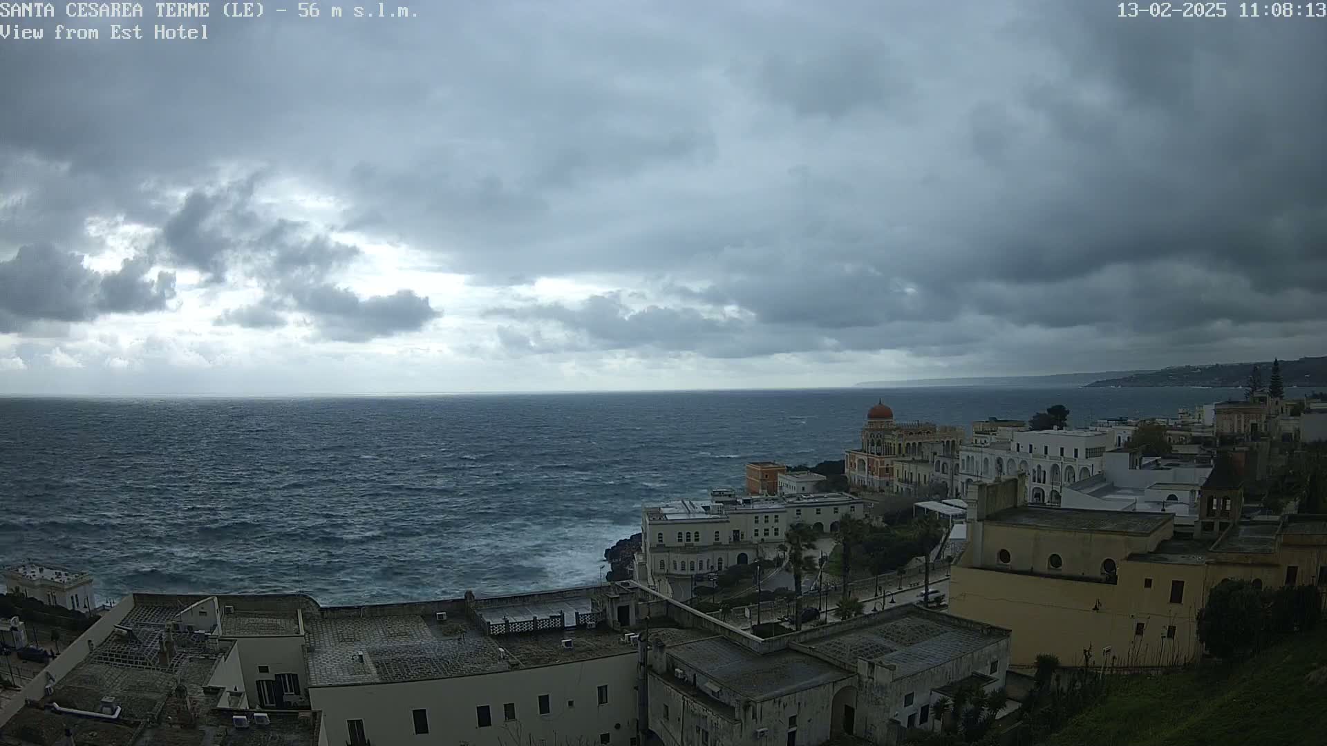 A coastal town with white buildings and a calm sea under a cloudy sky.