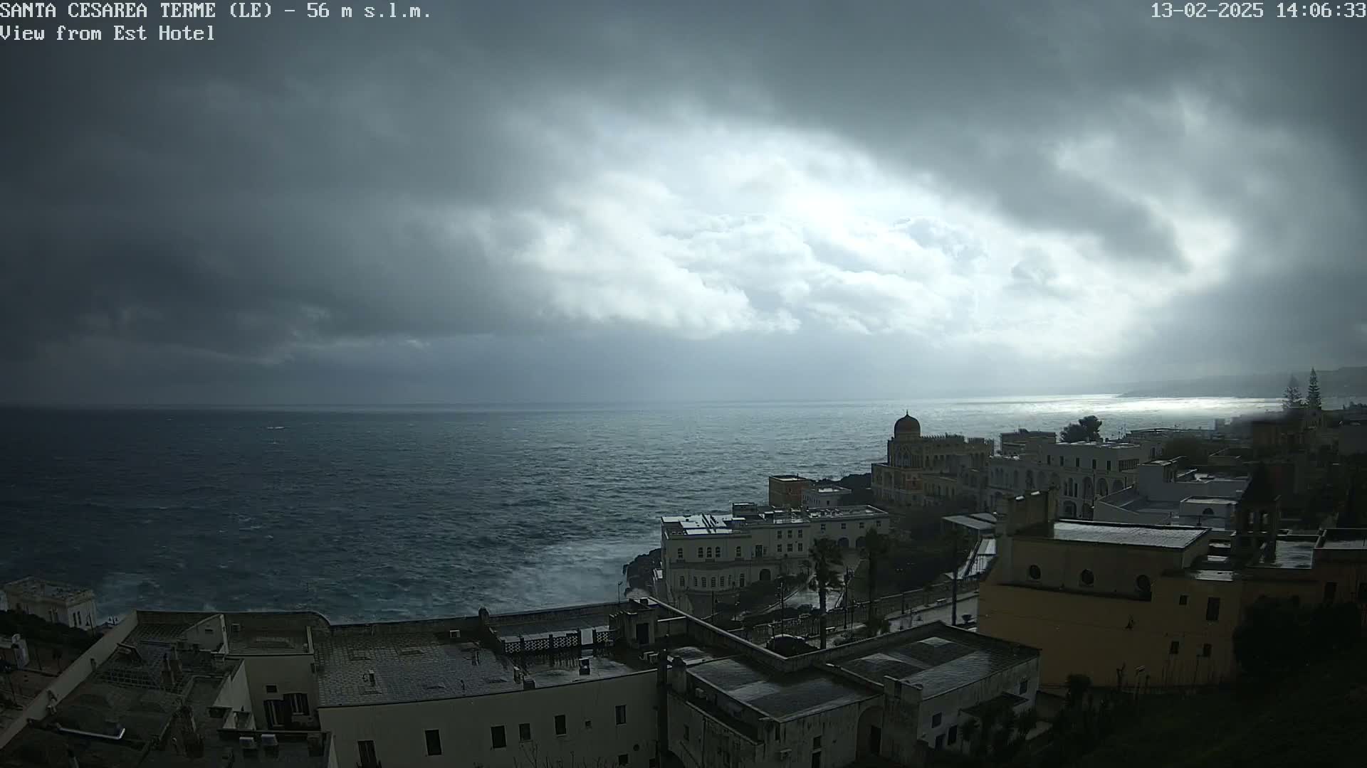 A coastal town with dark, stormy clouds overhead, and a rough sea visible in the distance.