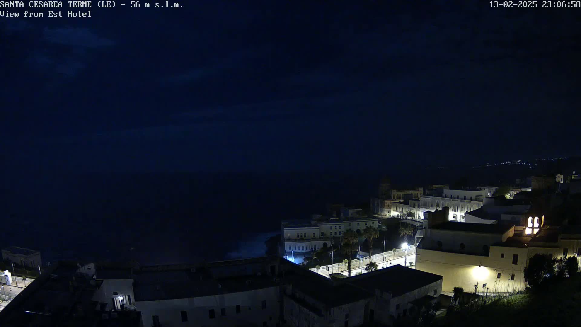 A nighttime coastal town with dimly lit buildings overlooks a dark ocean under a clear, dark sky.
