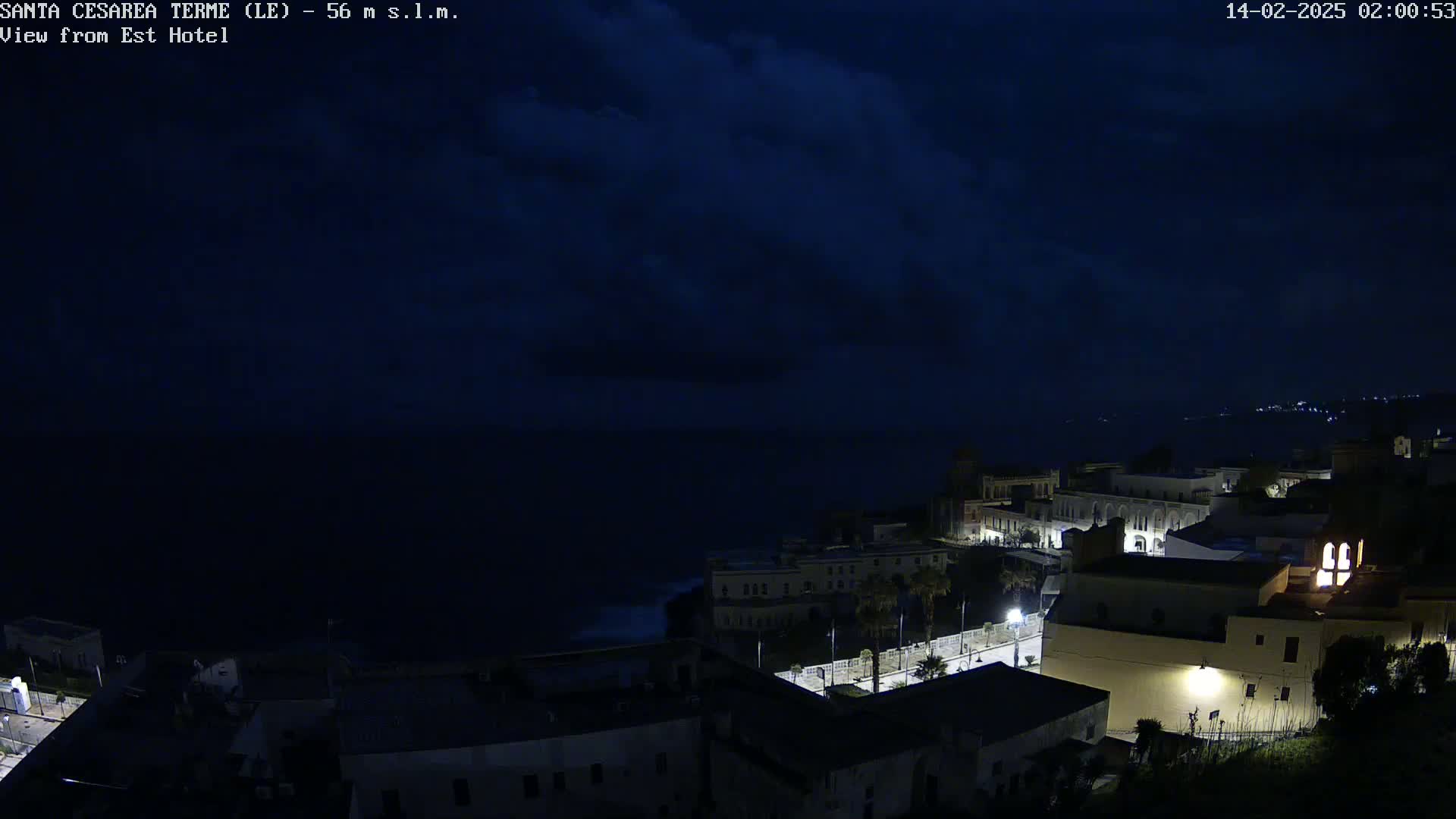 A nighttime coastal town overlooks a dark sea under a cloudy sky.