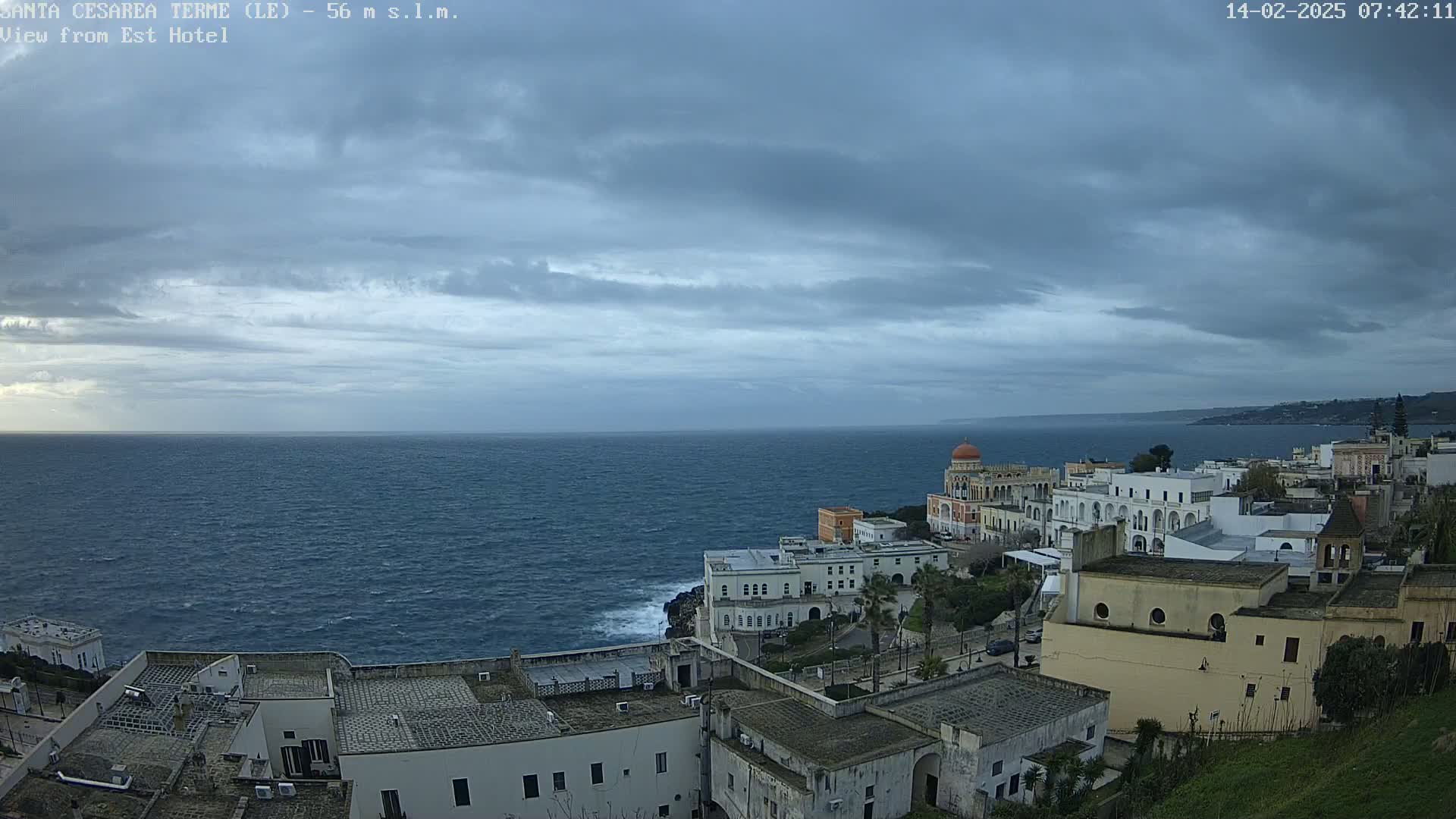 A coastal town with white buildings and a calm, dark-grey sea under a cloudy sky.