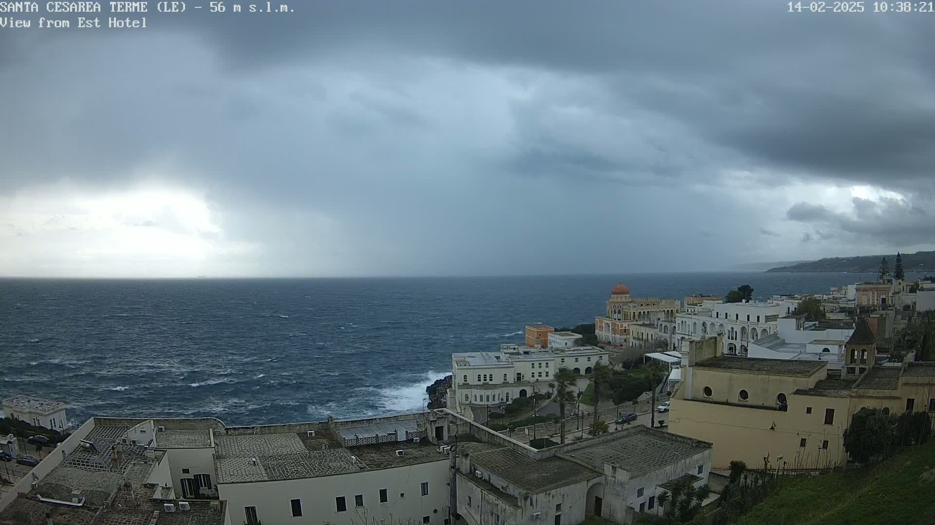 A coastal town with white buildings overlooks a choppy sea under a dark, cloudy sky.