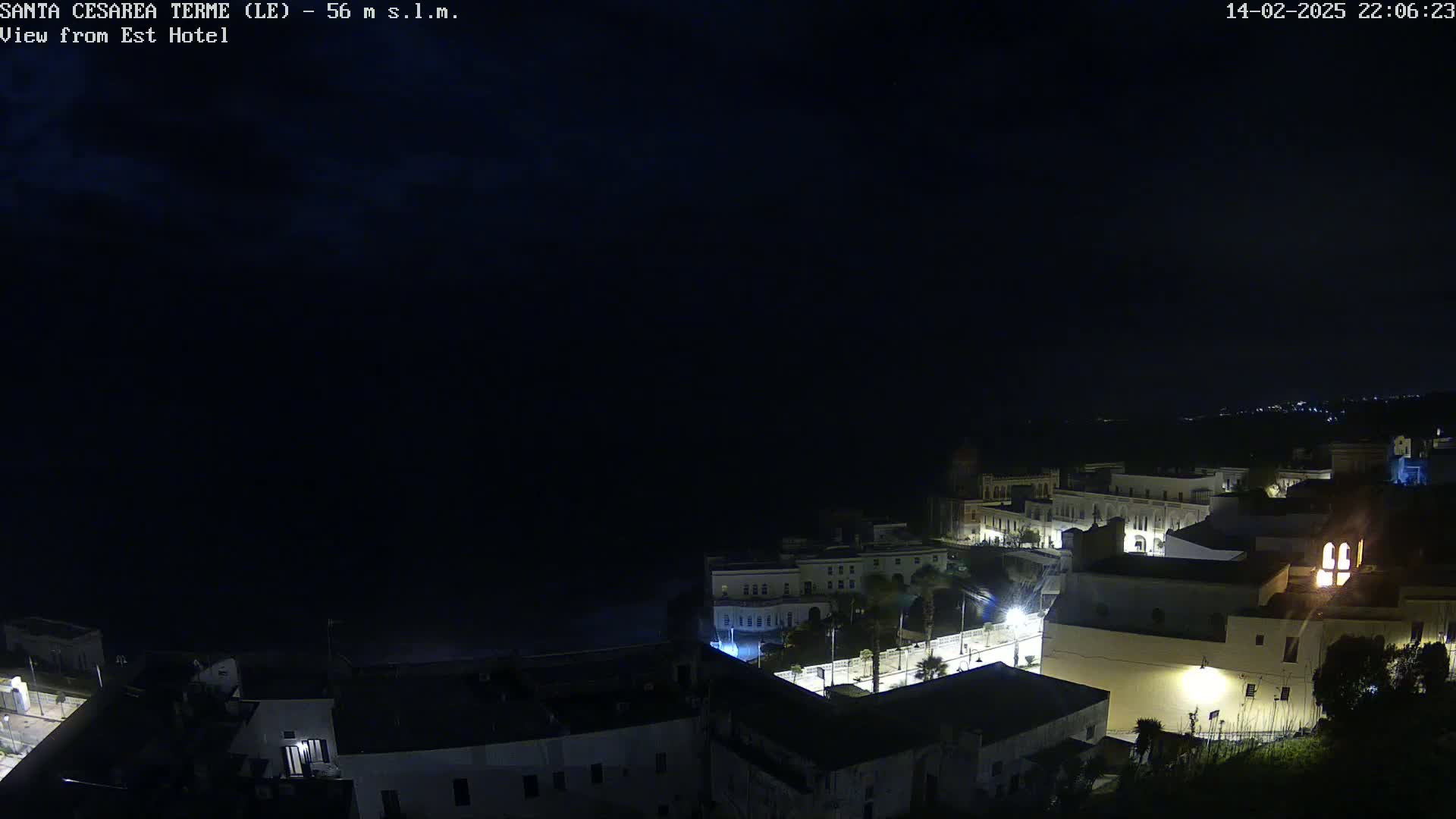 A nighttime view of a coastal town with dimly lit buildings and a dark, overcast sky.
