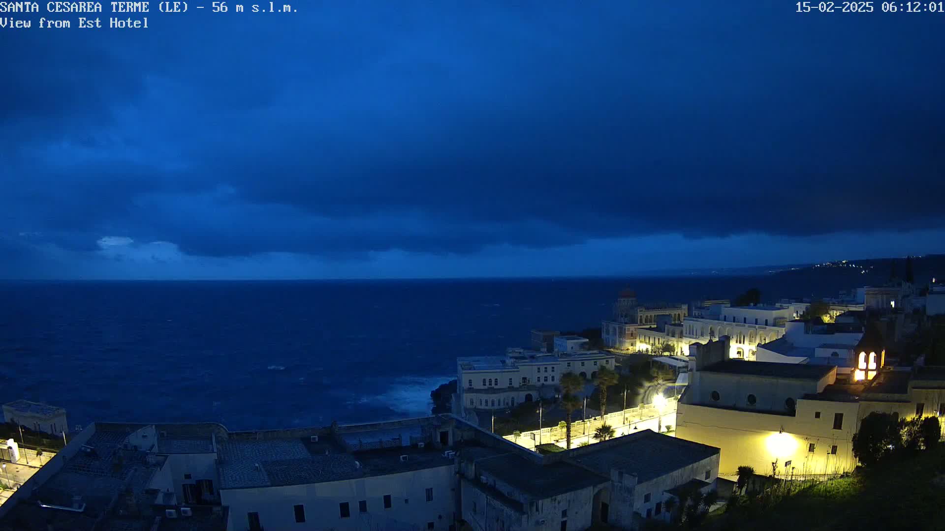 A coastal town at night under a dark, stormy sky, with waves crashing against the shore.