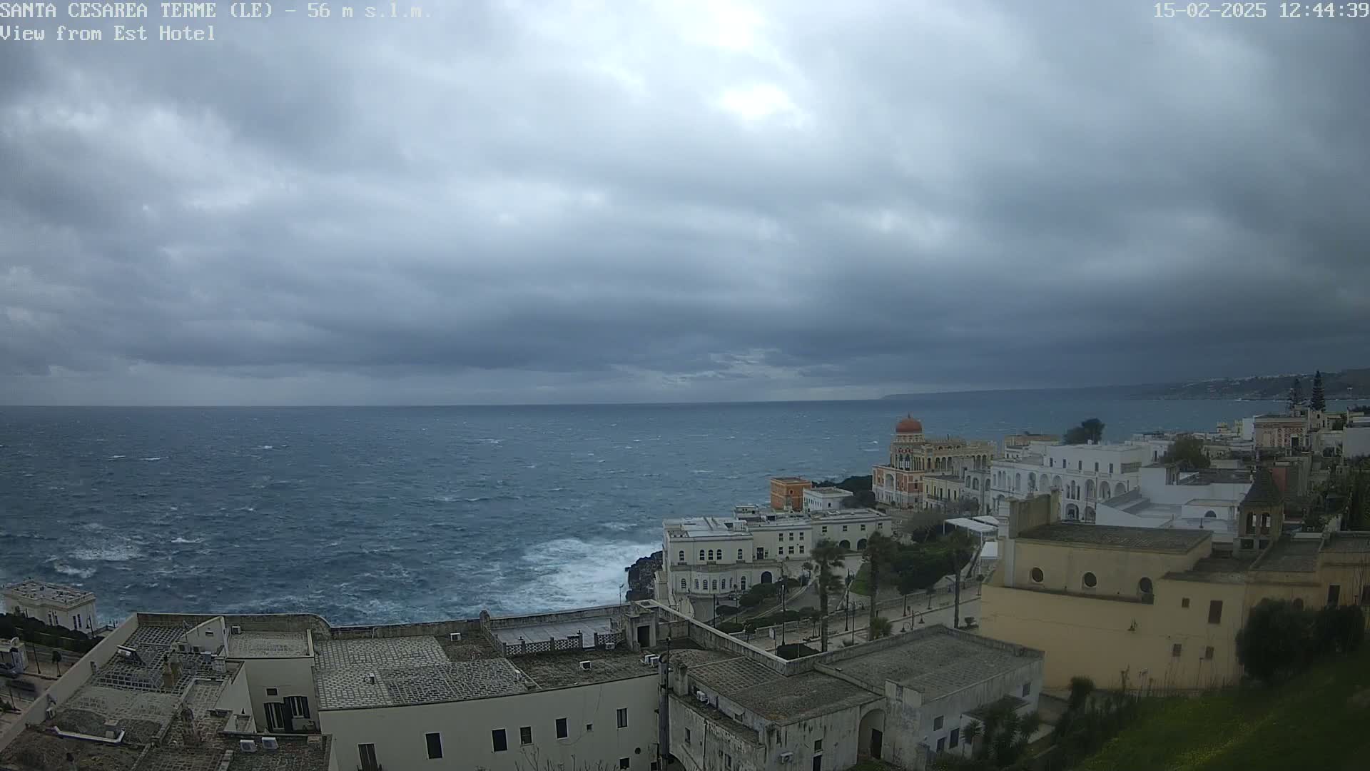 A coastal town with white buildings overlooks a choppy sea under a cloudy sky.