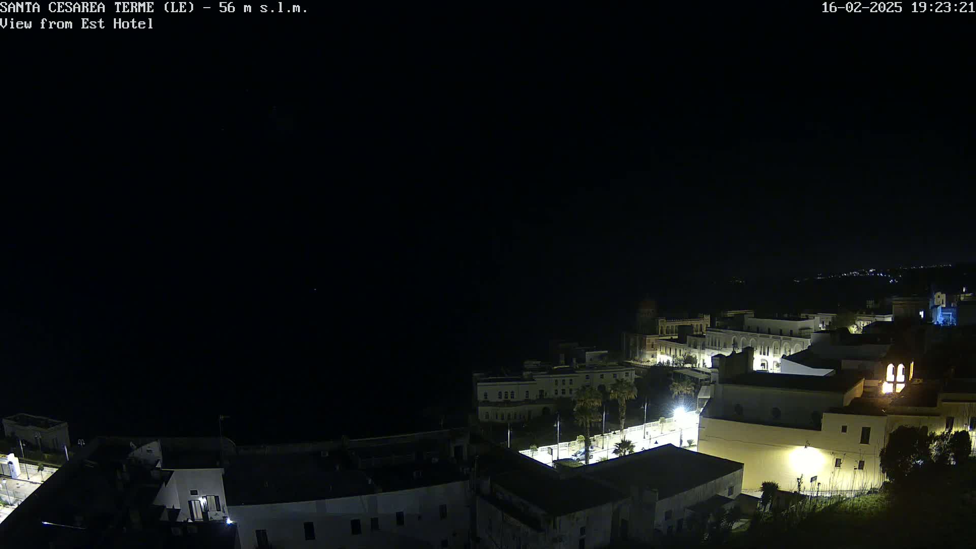 A nighttime, aerial view of a coastal town with buildings illuminated, under a clear, dark sky.
