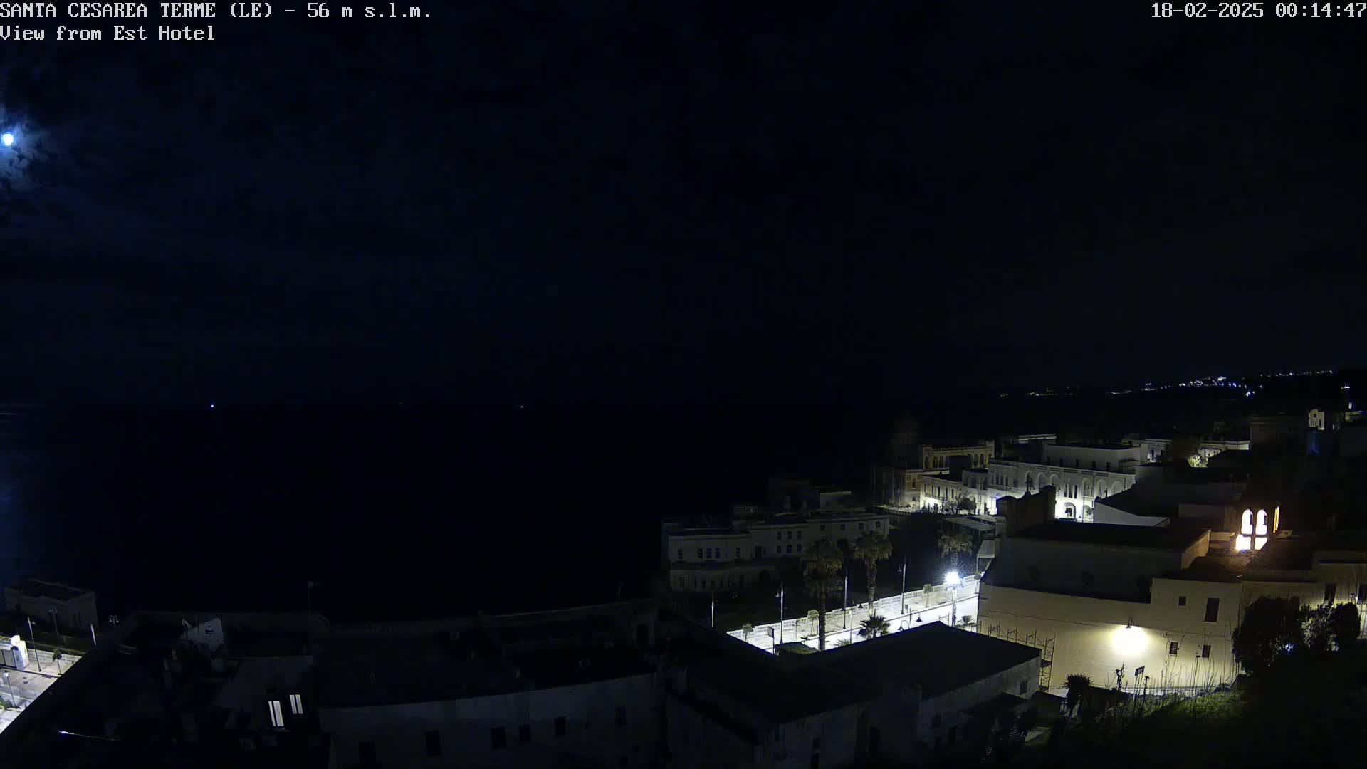 A nighttime, long shot of a coastal town overlooking a dark sea under a moonlit sky.
